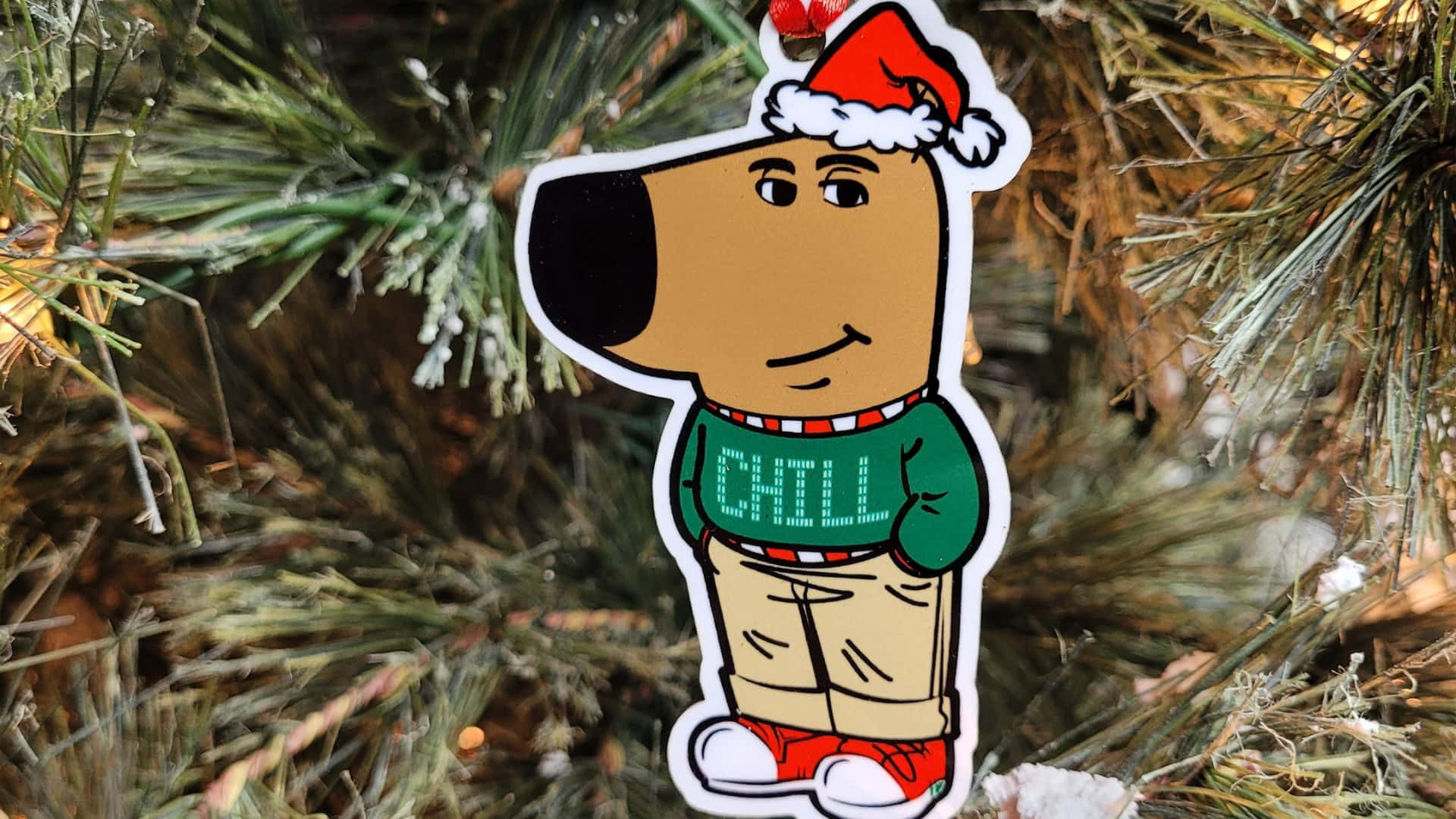  壁紙 — 一張卡通狗貼紙，戴著聖誕帽和「CHILL」毛衣，掛在雪松樹枝上。