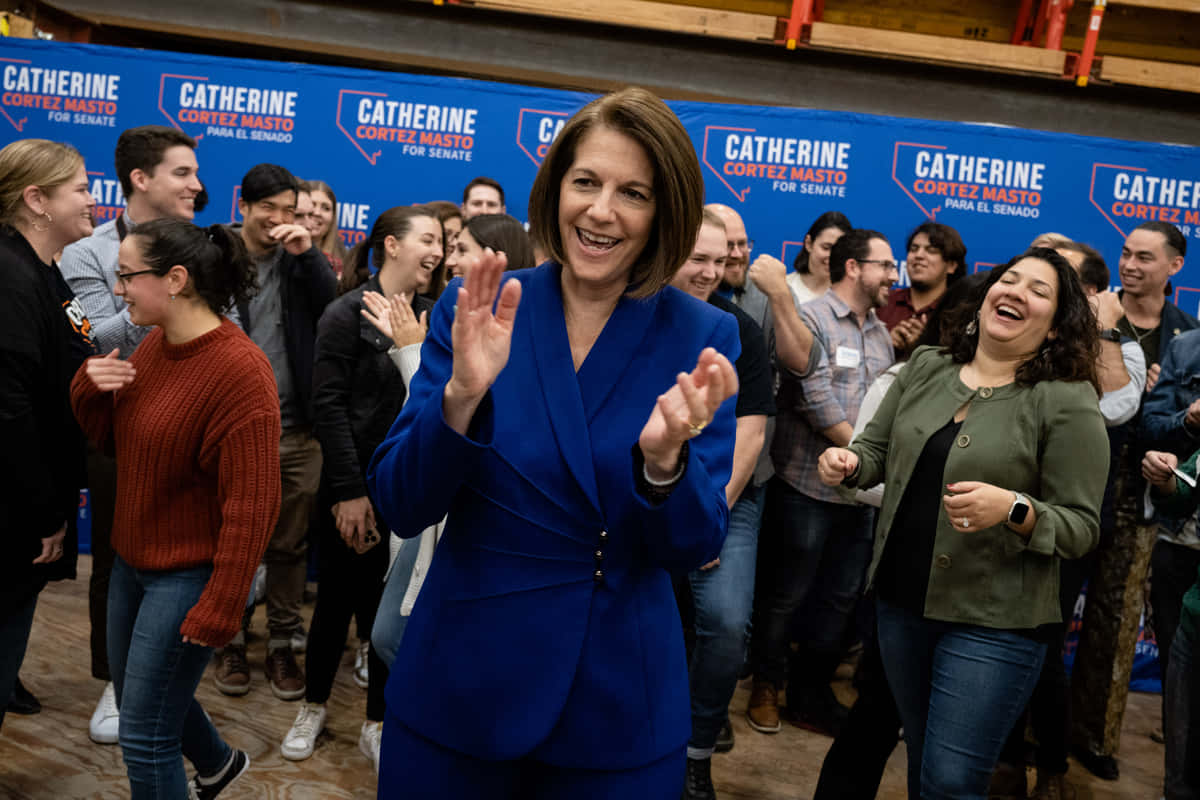 政治 桌布 壁紙 — Catherine Cortez Masto 在一個充滿活力的藍色背景的競選活動中，熱情地向支持者揮手。