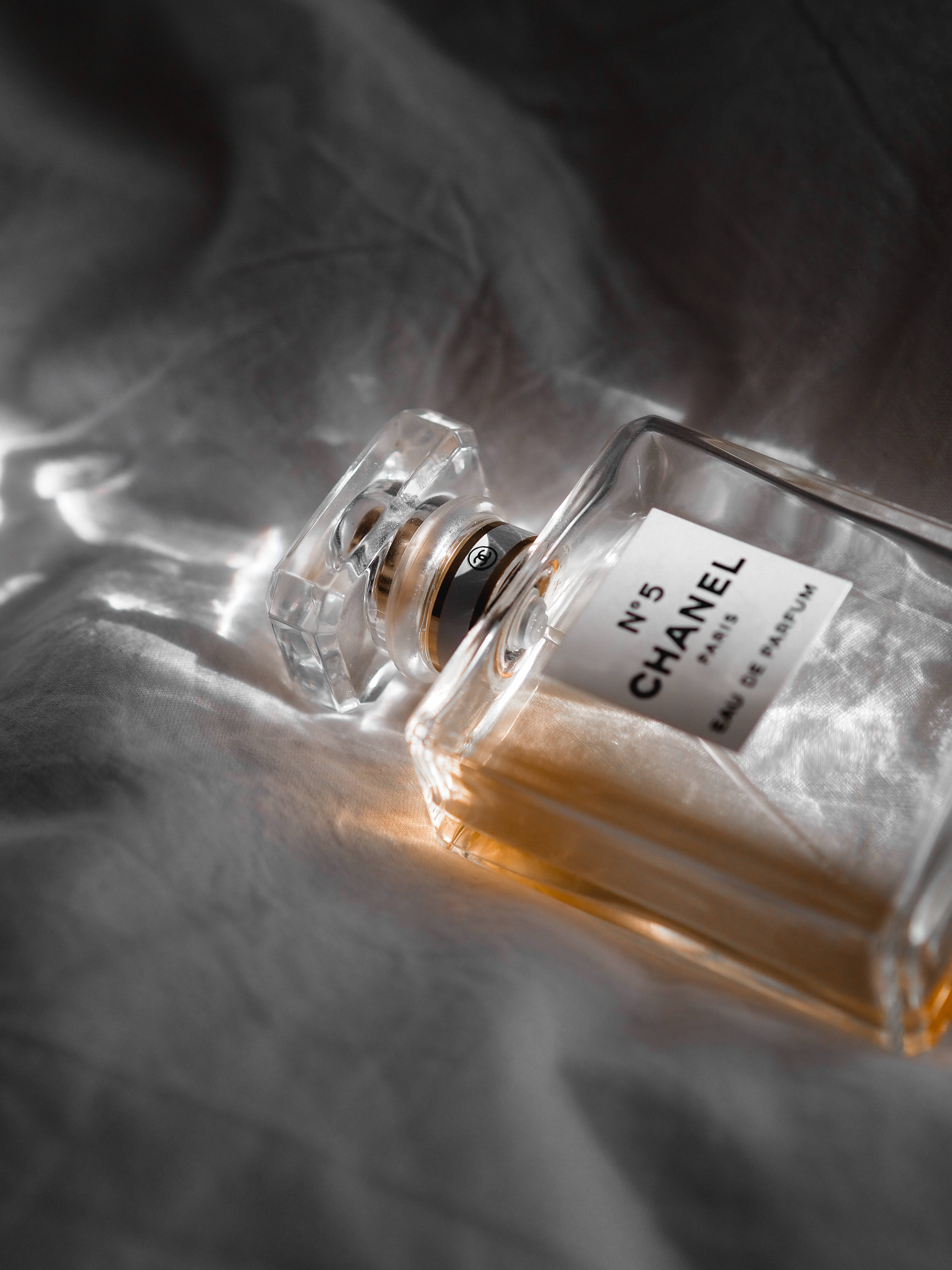 Chanel 桌布 壁紙 — Chanel No 5 香水瓶放在皺巴巴的灰色布料上，沐浴在柔和的金色光線中，突顯其標誌性的方形瓶身和琥珀色液體。