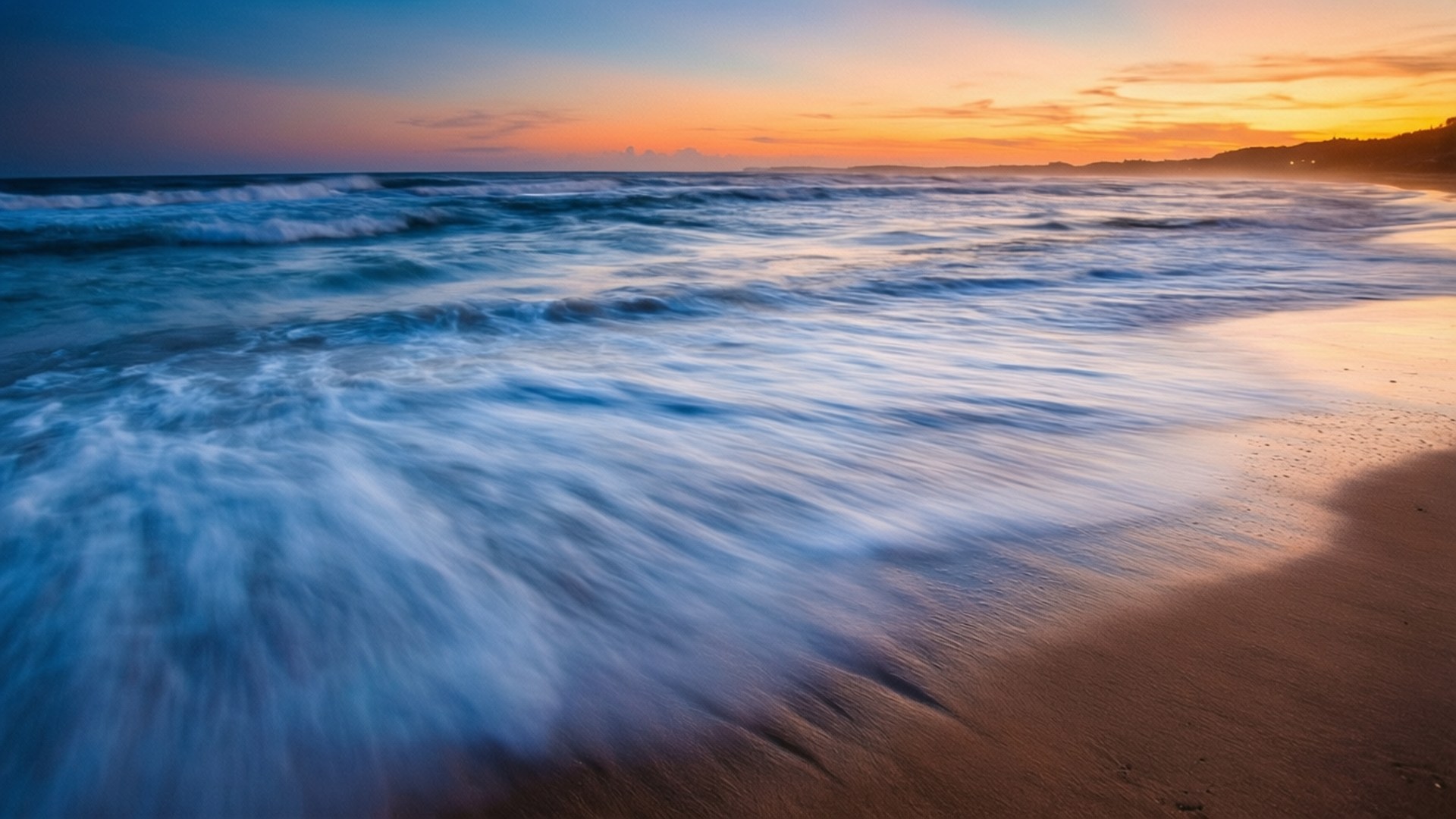 Long Exposure Sunset Waves 壁紙 — 長時間曝光捕捉到絲滑的藍色海浪沖刷著金色沙灘，在充滿活力的日落時分。