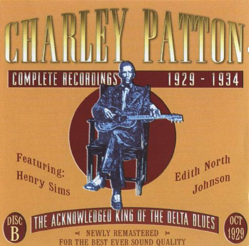 Legend 桌布 壁紙 — Charley Patton 坐著吉他的復古專輯封面，背景為溫暖的橙色，配以粗體字體。