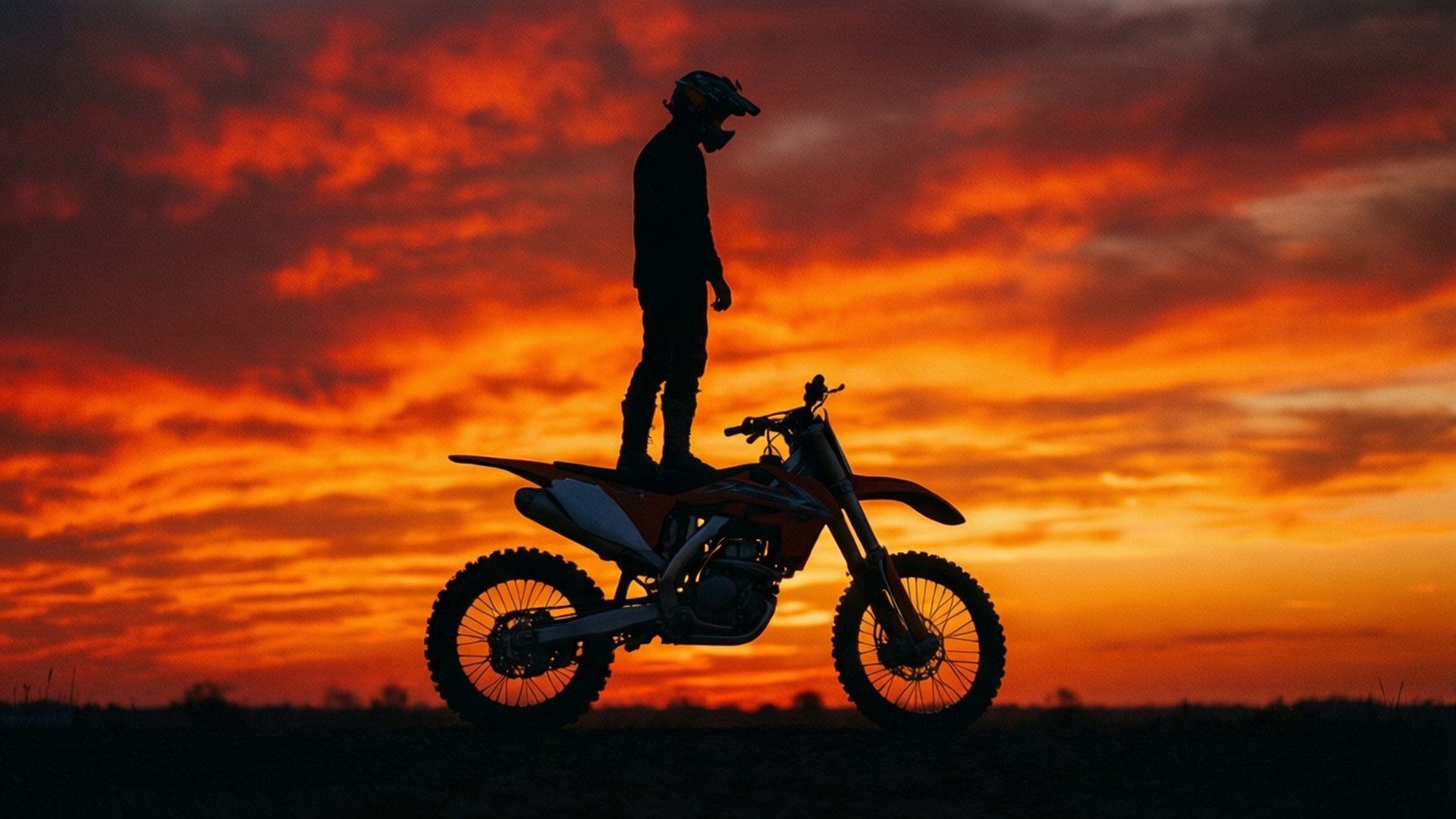 Silhouette Sunset Stunt 壁紙 — 一名車手站在越野機車上，在熾熱的橙紅色日落天空下形成剪影。