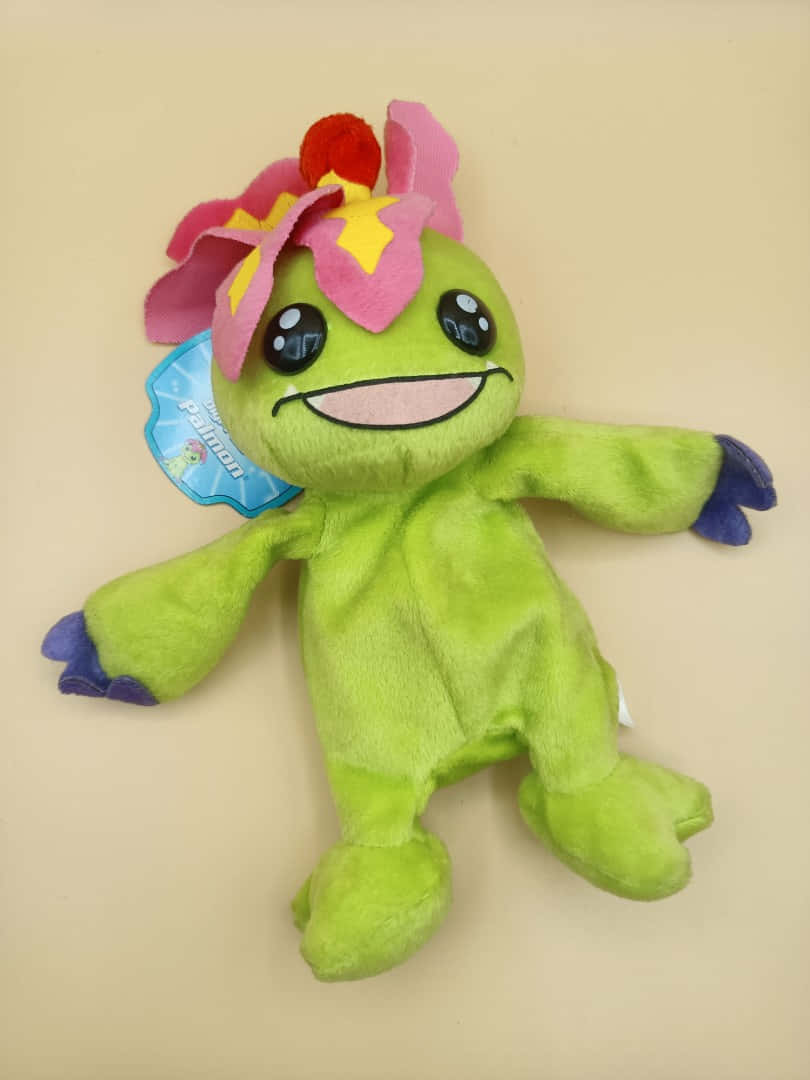 Digimon Palmon 桌布 壁紙 — 一個快樂的綠色毛絨玩具，戴著粉紅色花帽和藍色手，平躺在米色背景上。