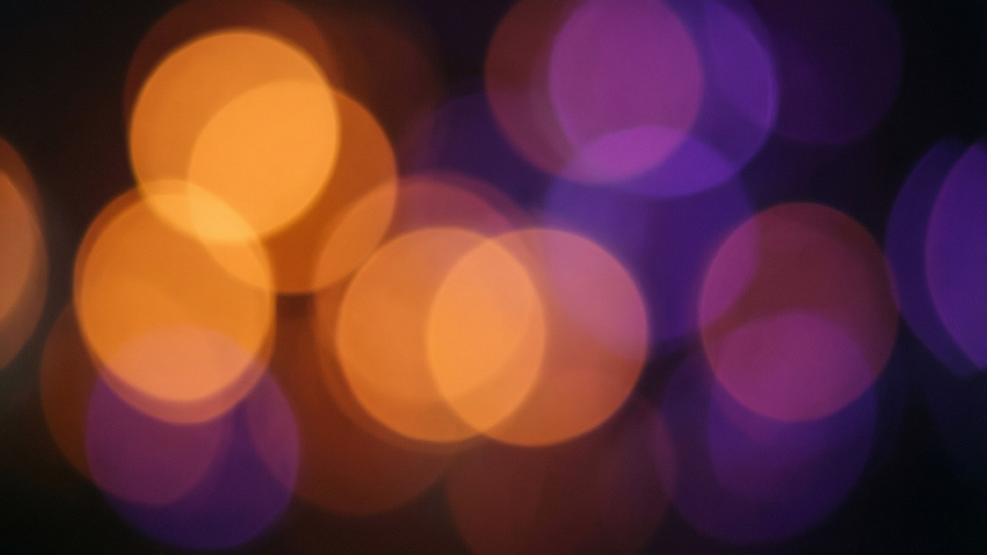 macOS Mojave Bokeh Dream 壁紙 — 橙色和紫色光的柔和發光球體在黑暗背景上模糊，營造出夢幻般的散景效果。