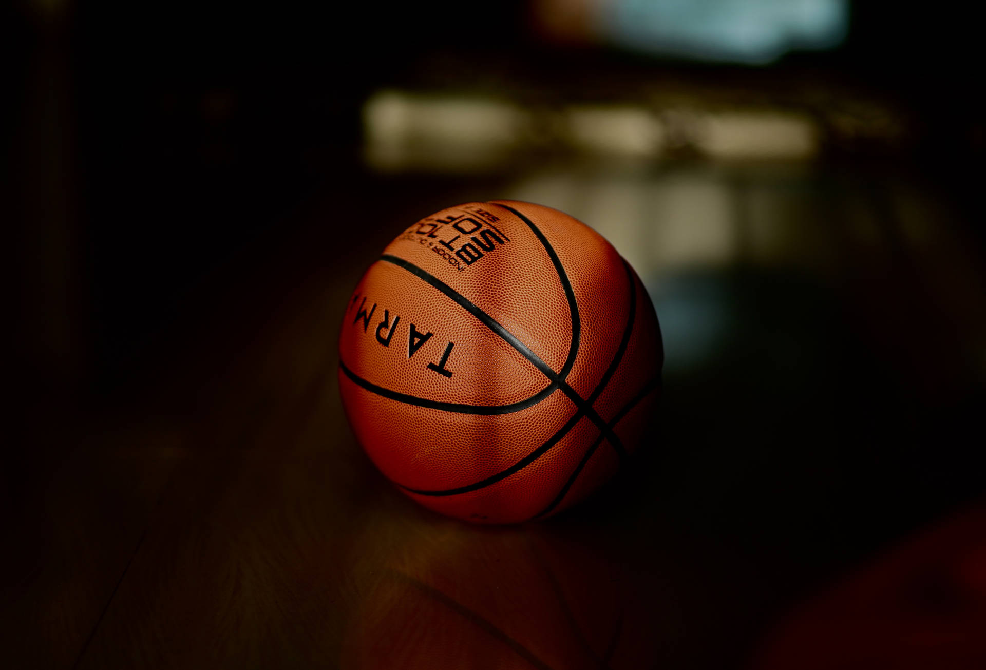 一個橙色籃球放在昏暗房間的木地板上。 — NBA 壁紙
