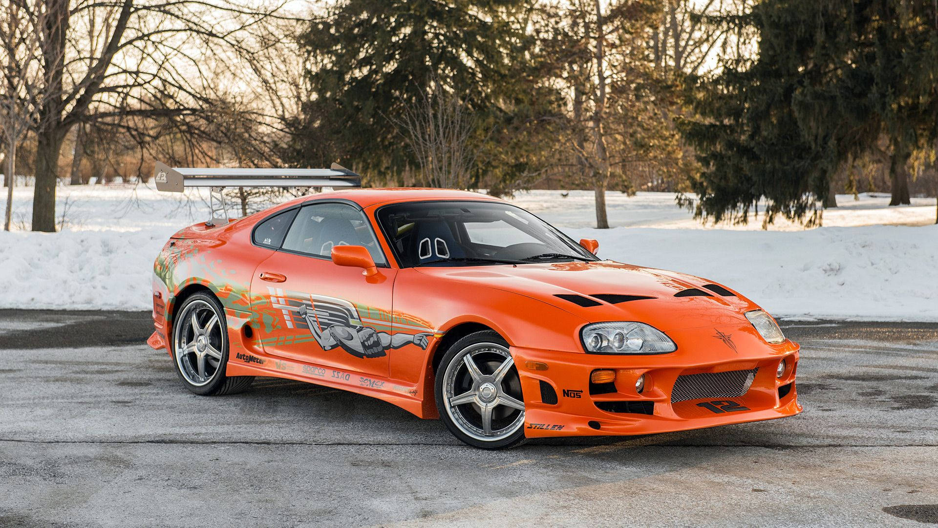 橙色豐田Supra跑車停放在積雪瀝青上，背景有光禿禿的樹木。 — Toyota Supra 壁紙