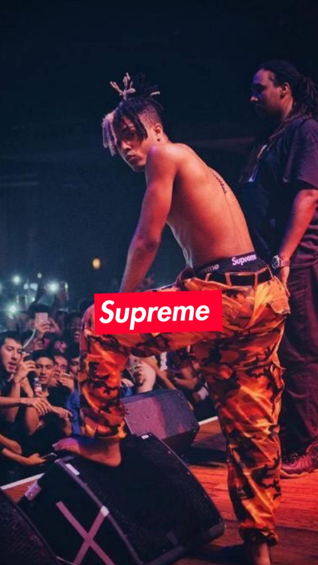 赤裸上身的表演者穿著橙色迷彩褲在舞台上，觀眾正在觀看 — Xxxtentacion 壁紙