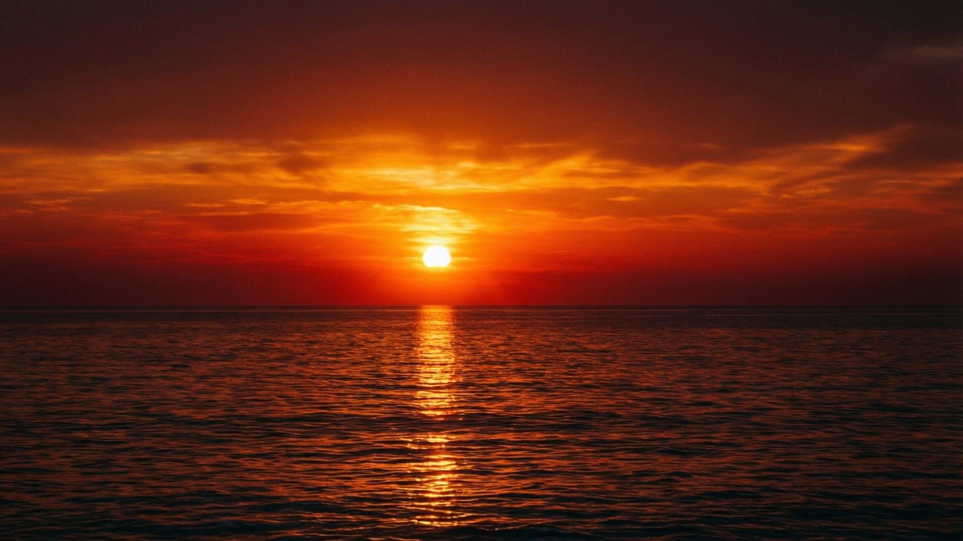 Sunset Sea Reflection 壁紙 — 熾熱的橙色夕陽落在平靜的海面上，在漸暗的海上投射出一條閃爍的金色路徑。