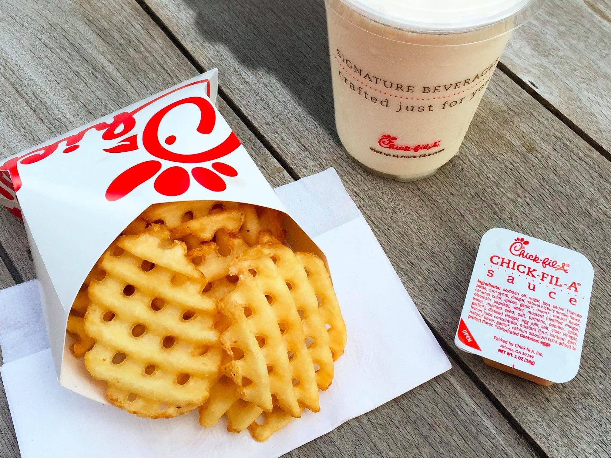 chick 桌布 壁紙 — Chick-fil-A 盒子裡的金黃色格子薯條，旁邊放著招牌飲料和醬料包，置於經風化的木桌上。