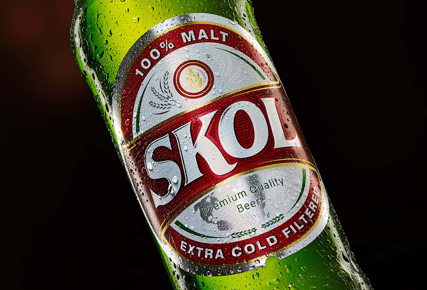  壁紙 — 冰涼的綠色Skol啤酒瓶在深色背景下閃爍著冷凝水珠。