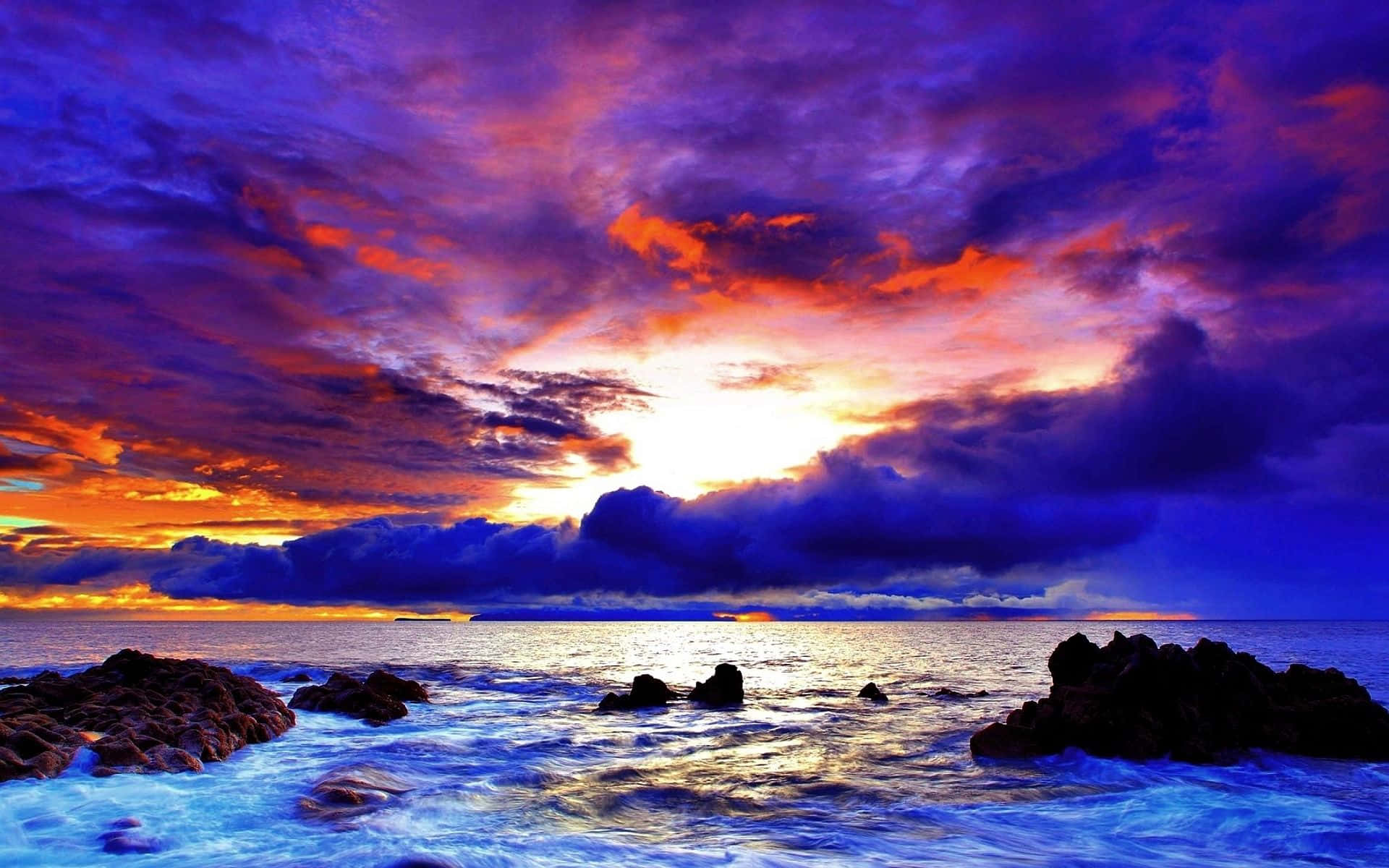 Coastal Sunset 桌布 壁紙 — 充滿活力的紫色、橙色和藍色日落雲彩在岩石海洋海岸線上閃耀，伴隨著拍岸的波浪。