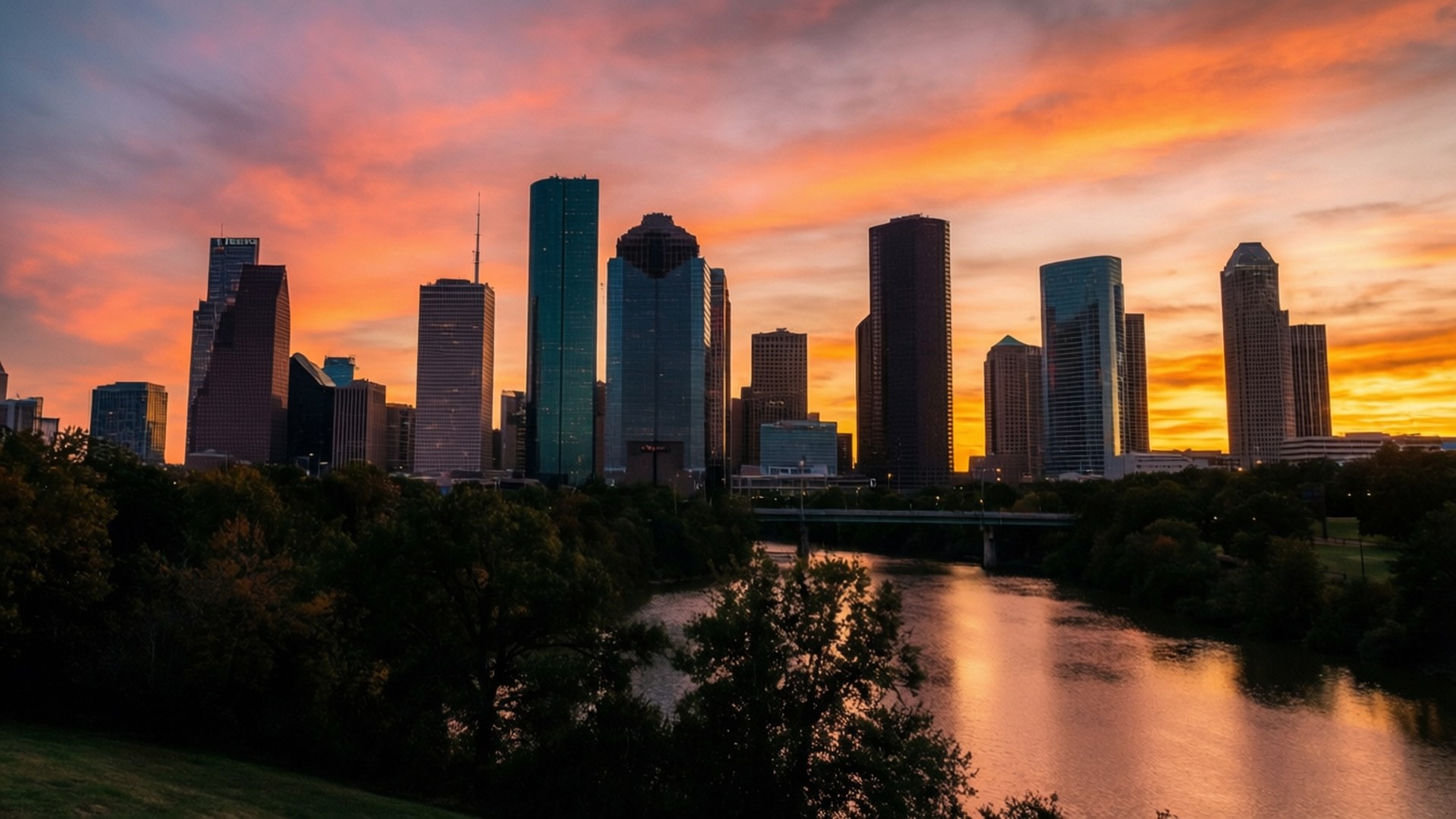 Houston Sunset Skyline 壁紙 — 充滿活力的日落將休士頓天際線染成火熱的橙色和粉紅色調，倒映在下方平靜的河流上。