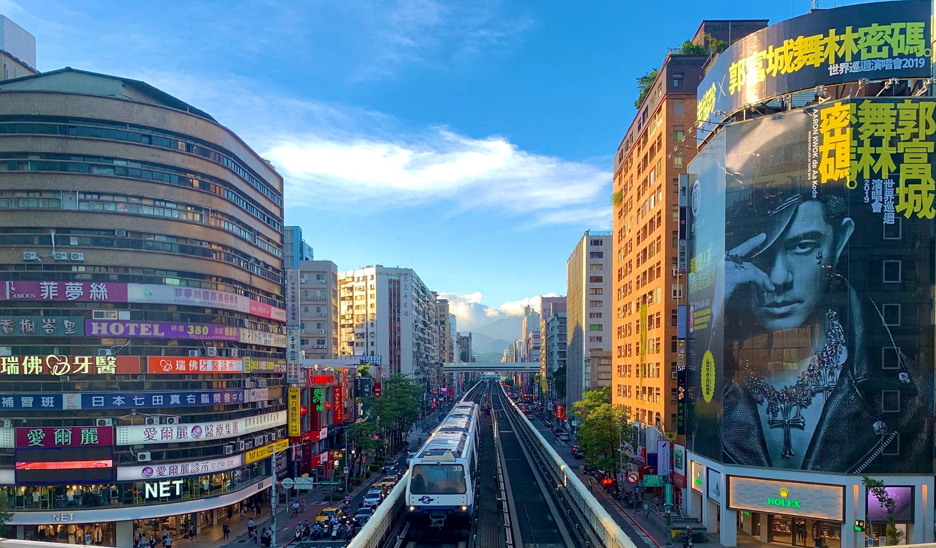 單軌列車行駛在繁華的城市街道上，兩旁是高樓大廈和色彩繽紛的招牌。 — 台北 壁紙