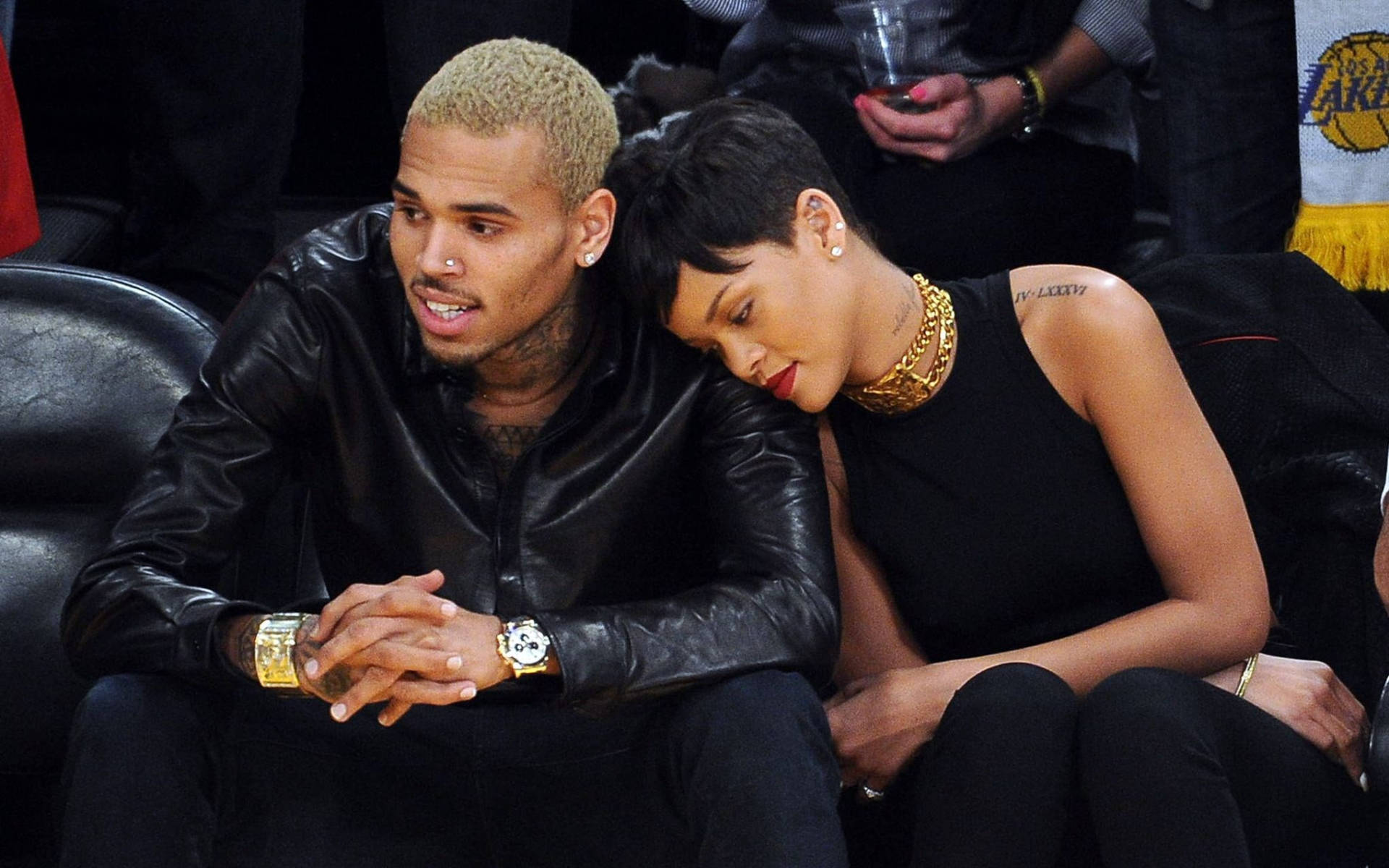 Chris Brown 桌布 壁紙 — Chris Brown 和 Rihanna 在籃球賽中緊貼著坐在黑色皮革座椅上，她的頭靠在他的肩膀上。