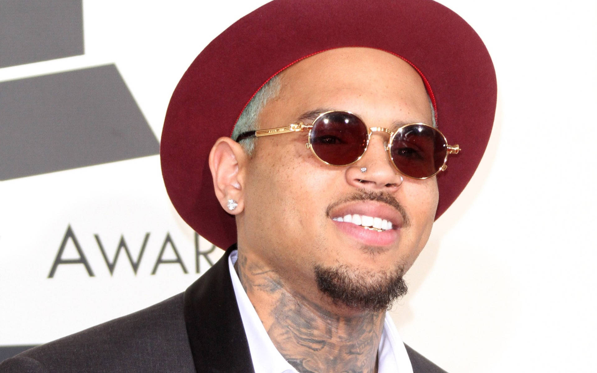 Chris Brown 桌布 壁紙 — Chris Brown 在葛萊美獎上自信微笑，戴著栗色帽子、金色邊框太陽眼鏡和黑色西裝。