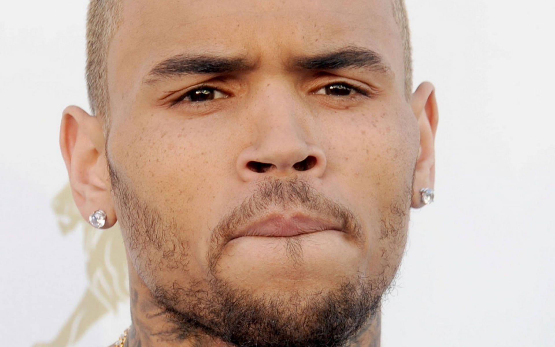 Chris Brown 桌布 壁紙 — Chris Brown 戴鑽石耳環、表情嚴肅的特寫肖像，背景是明亮的白色。