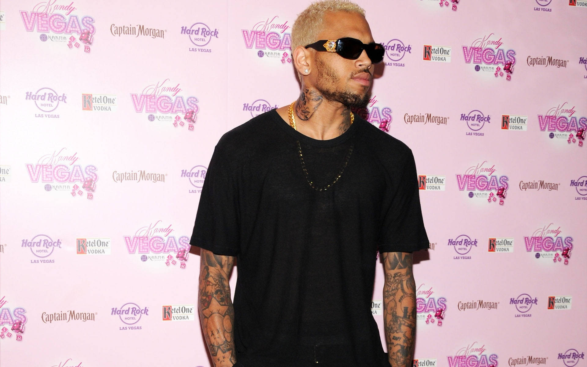 Chris Brown 桌布 壁紙 — Chris Brown 自信地穿著黑色服裝和太陽眼鏡，在粉紅色的品牌活動背景前擺姿勢。