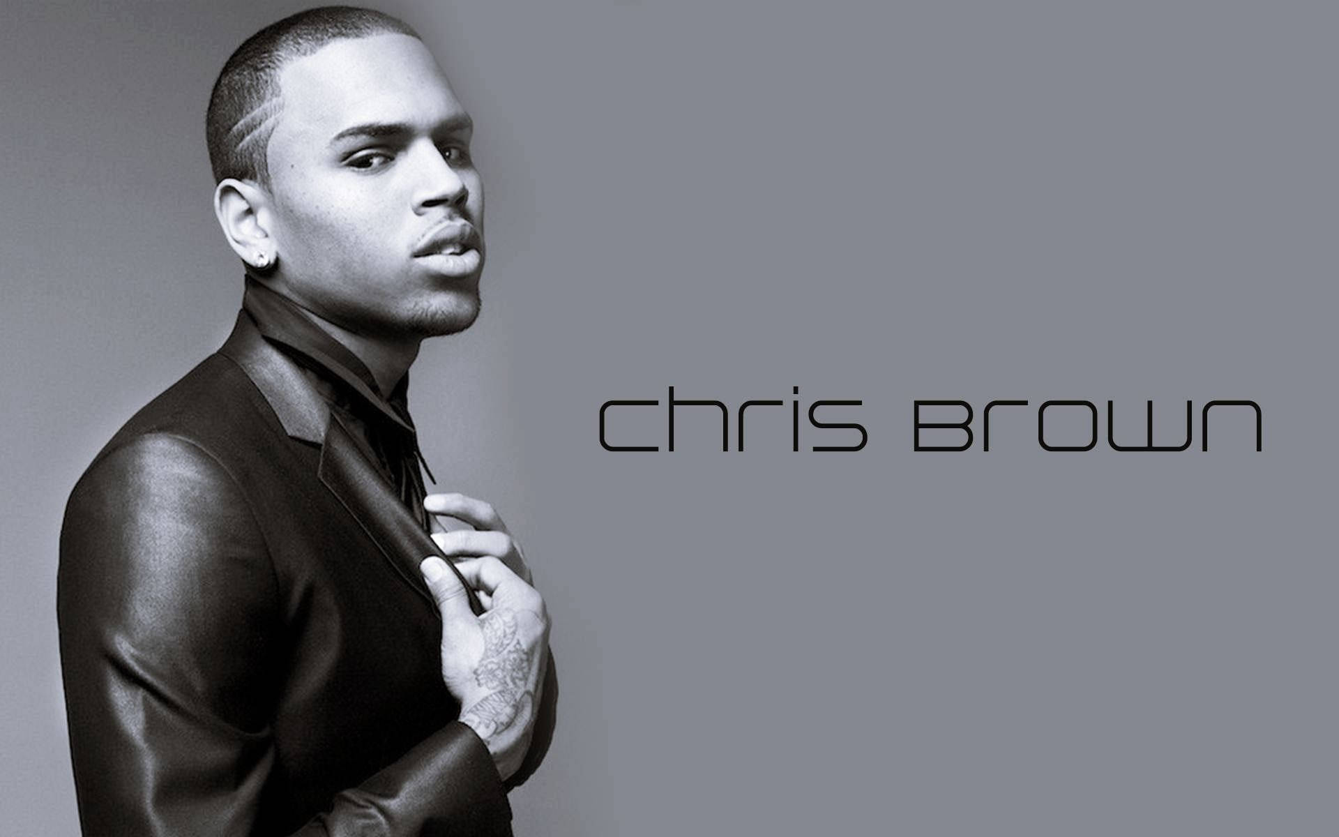 Chris Brown 桌布 壁紙 — Chris Brown身穿時尚黑色皮夾克，在簡約灰色背景前自信擺姿勢，他的名字優雅地寫在旁邊。