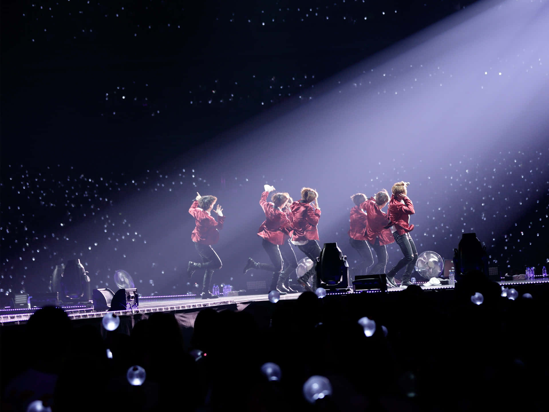 Bts Stage 桌布 壁紙 — 穿著紅色外套的表演者在音樂會舞台上，在聚光燈光束下，於飄落的閃粉中充滿活力地跳舞。