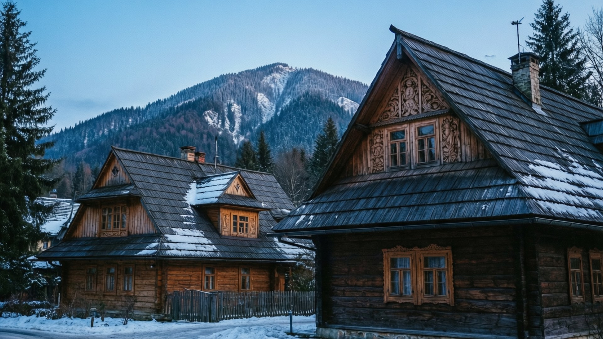 Zakopane Winter Architecture 壁紙 — 傳統木屋頂上覆蓋著雪，矗立在晴朗藍天下高聳的雪山前。