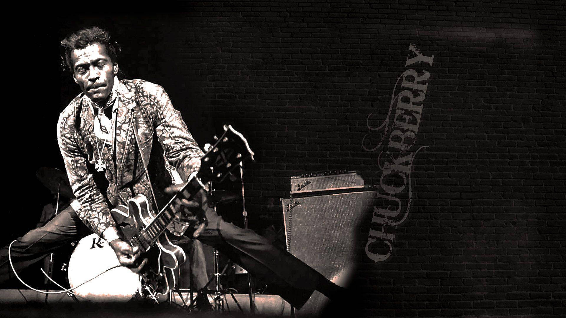 Chuck Berry 在舞台上彈吉他，背景是磚牆，他的名字被寫出來。 — 吉他動圖 壁紙