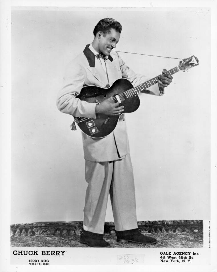 吉他動圖 桌布 壁紙 — Chuck Berry 穿著淺色西裝，在簡單的攝影棚背景下微笑彈吉他。