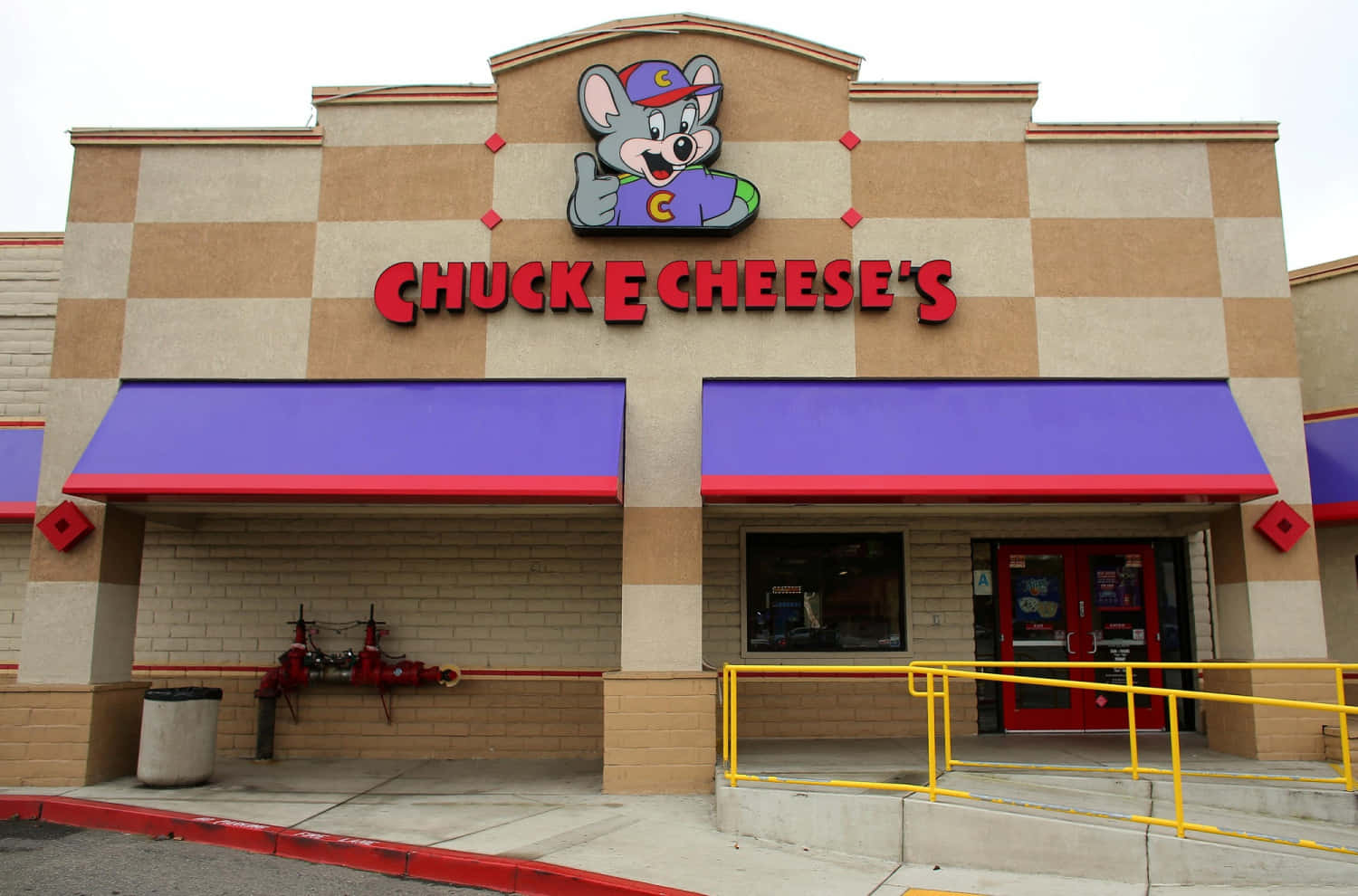 查克芝士 桌布 壁紙 — Chuck E Cheese's 餐廳外牆，紅色字樣上方有卡通老鼠吉祥物，紫色遮陽篷，陰天。