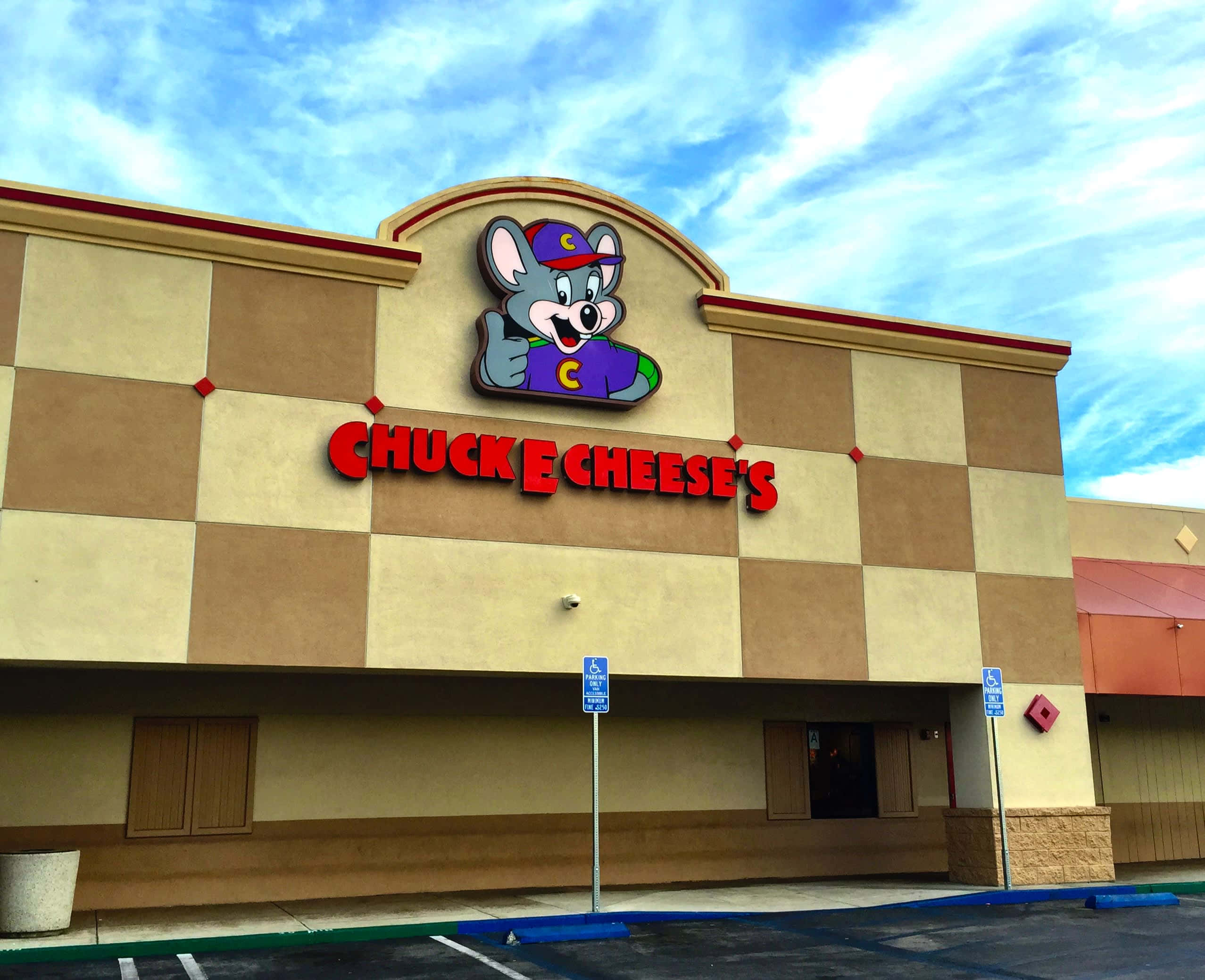 查克芝士 桌布 壁紙 — Chuck E Cheese's 街機餐廳，棋盤格外牆，卡通老鼠吉祥物，在明亮的藍天下。