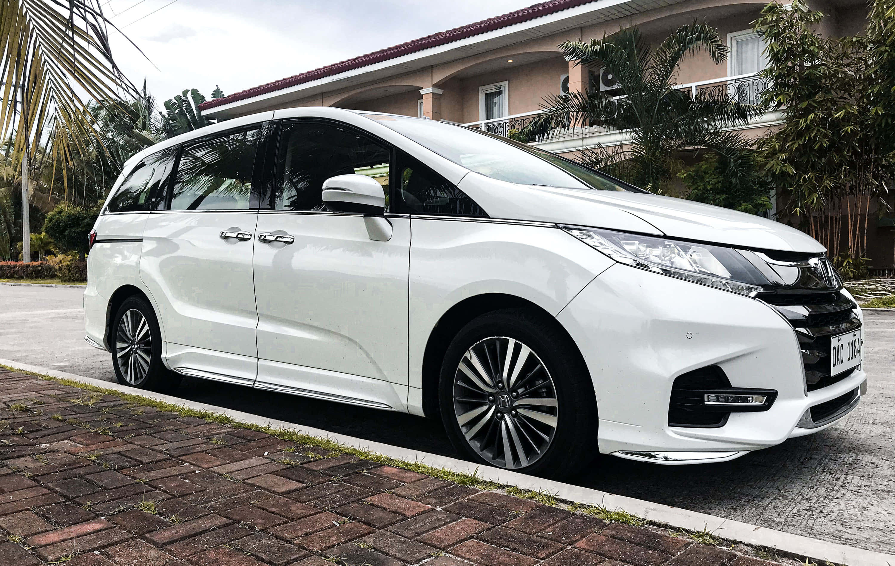 Honda Odyssey 桌布 壁紙 — 一輛純白色本田Odyssey廂型車停在磚砌車道上，旁邊是帶有棕櫚樹的熱帶房屋。