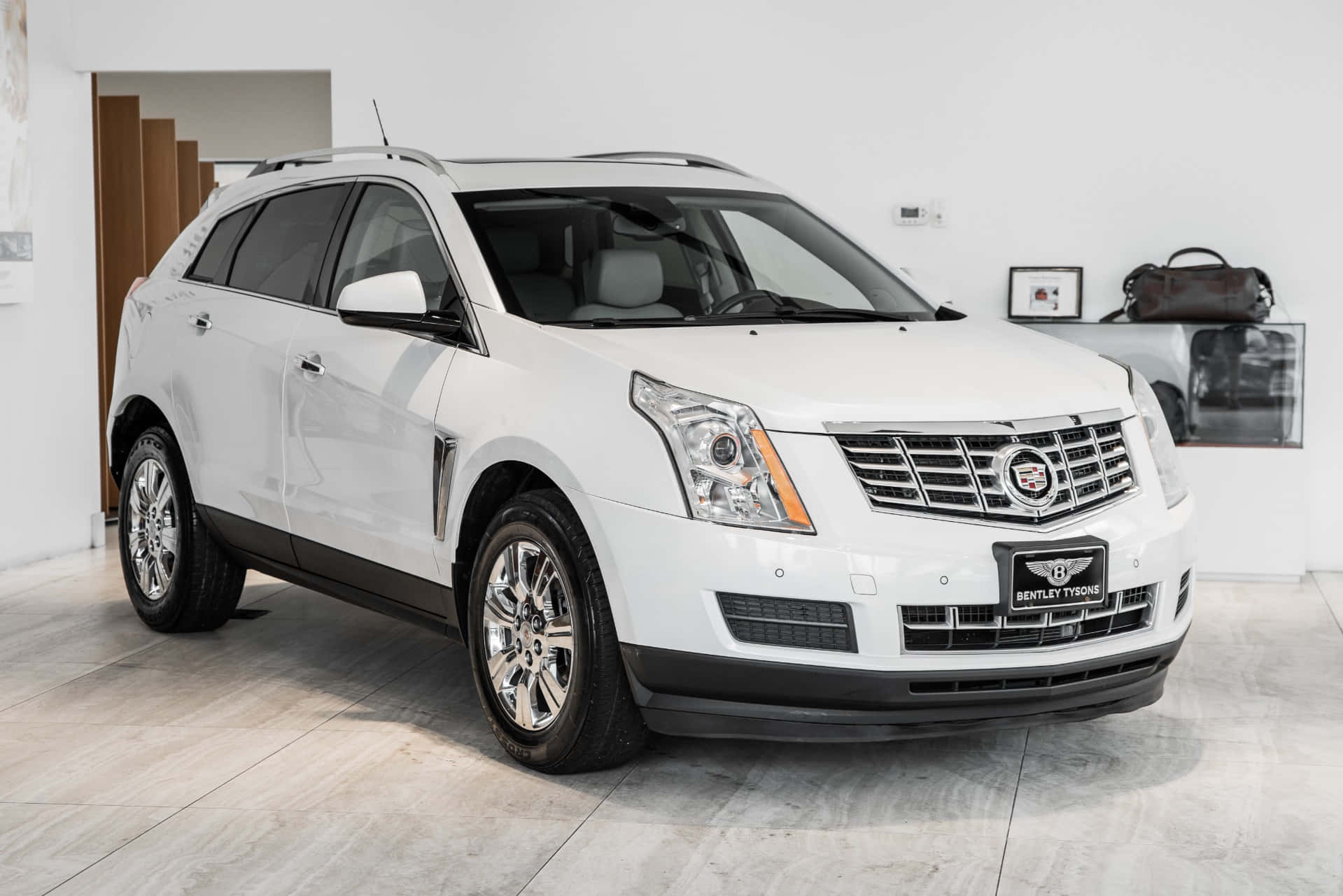 Cadillac Srx 桌布 壁紙 — 一輛純白色的凱迪拉克SUV在明亮的攝影棚燈光下，在一個帶有淺色木質裝飾和拋光混凝土地板的極簡豪華展廳中閃閃發光。