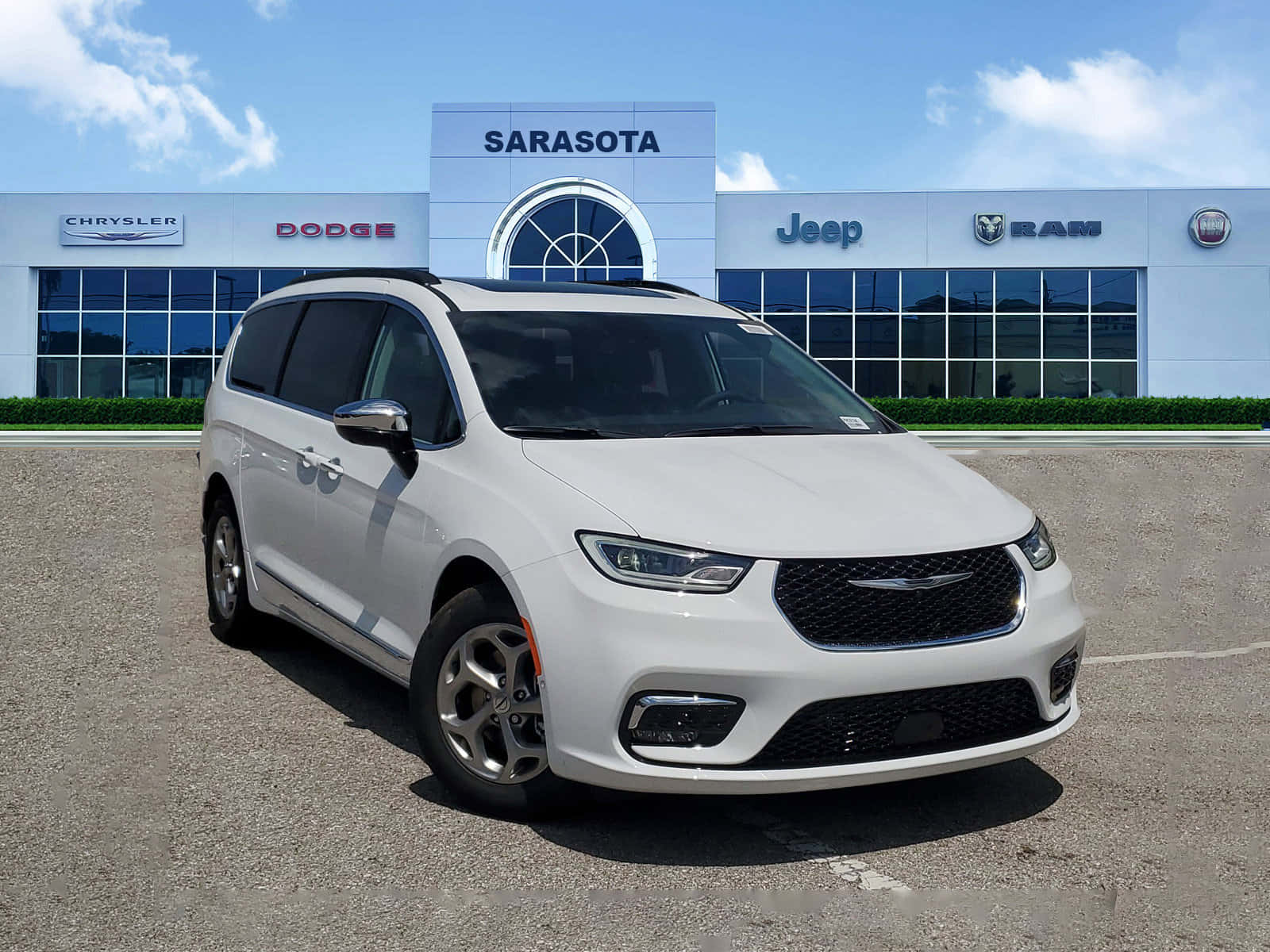 Chrysler Pacifica 桌布 壁紙 — 一輛純白色的 Chrysler Pacifica 小型貨車在明亮陽光下閃閃發光，停放在現代化經銷商前，上方是清澈的藍天。