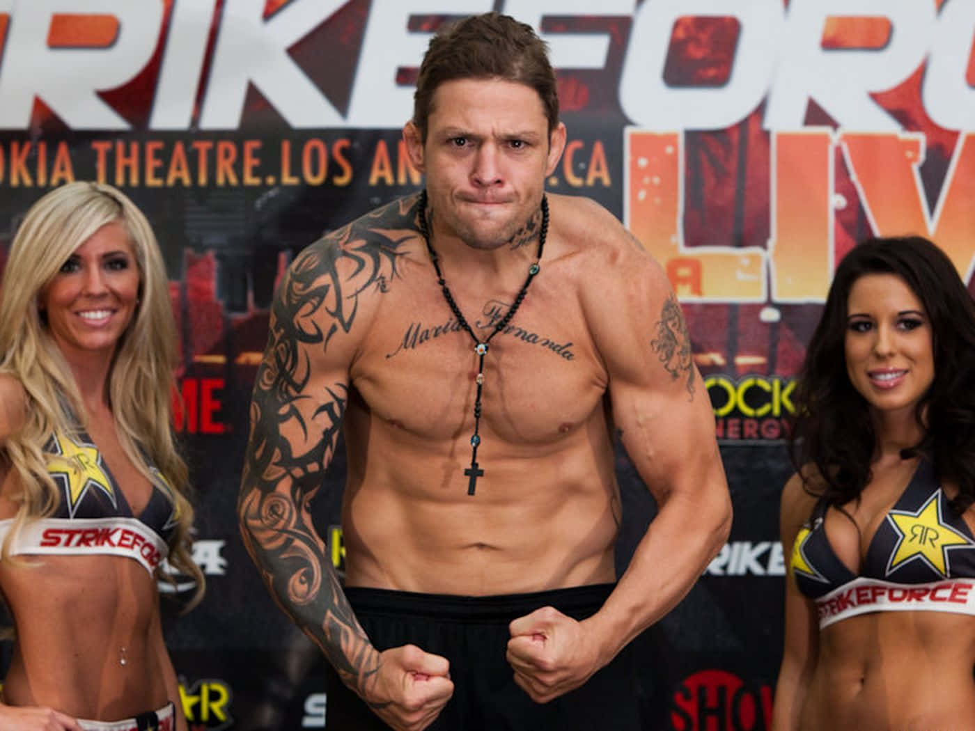 壁紙 — 一位刺青男拳手在Strikeforce稱重儀式上，在兩位微笑的舉牌女郎旁用力繃緊肌肉。