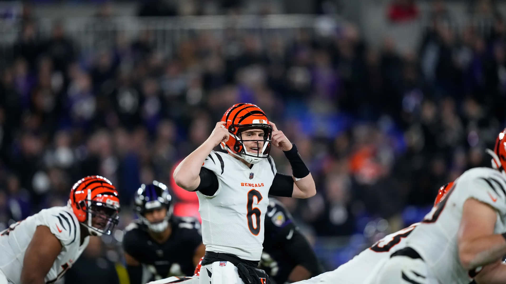  壁紙 — 一位身穿白色和橙色裝備的辛辛那提猛虎四分衛在夜間NFL比賽中，於球場燈光下調整頭盔。
