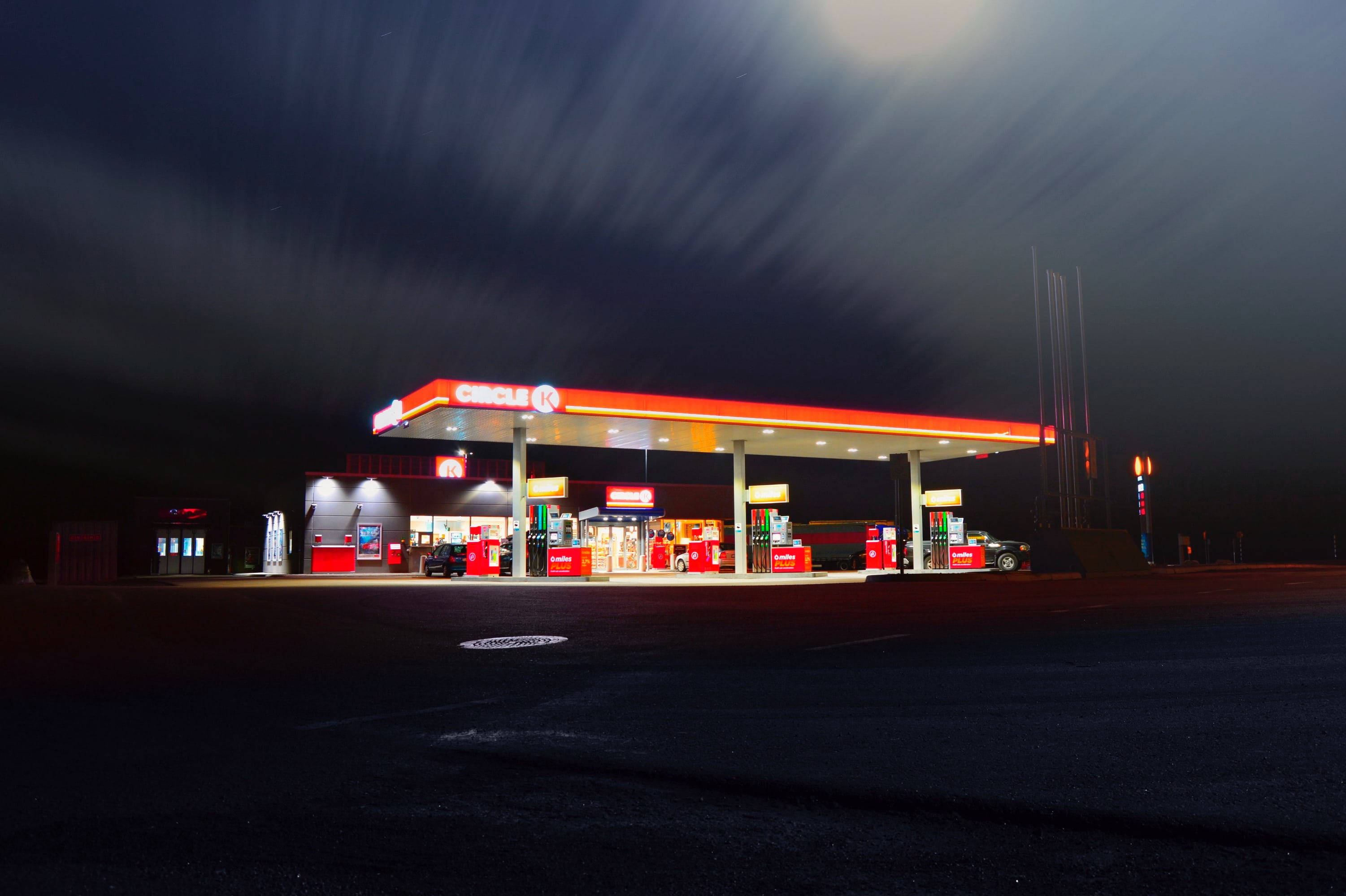 Gas Station 桌布 壁紙 — Circle K 加油站在繁星點點的夜空下發光，帶有條紋雲和長時間曝光產生的動態模糊。