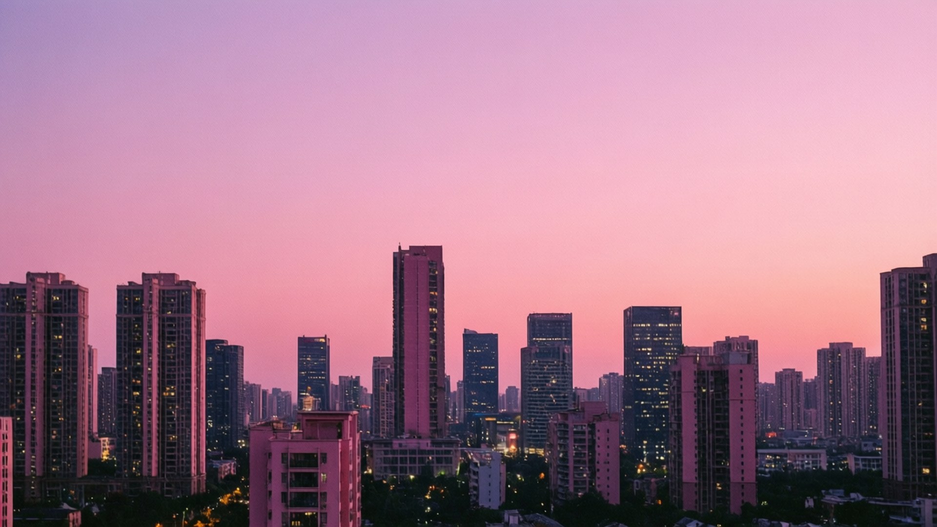 City Dusk 壁紙 — 黃昏時分的城市天際線沐浴在柔和的粉紅色和紫色色調中，點亮的窗戶在漸暗的天空中閃耀。