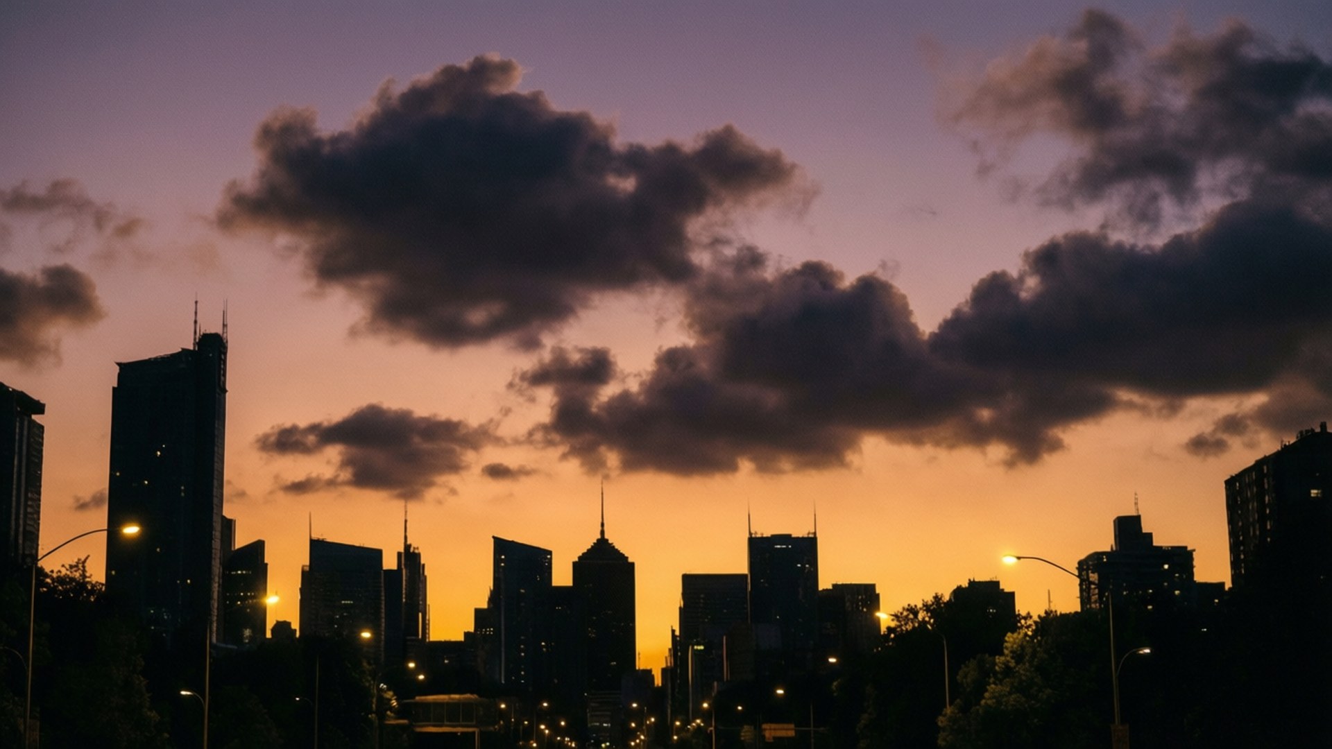 City Silhouette Clouds 壁紙 — 城市天際線在充滿活力的日落襯托下形成剪影，帶有紫橙色雲彩和發光的街燈。