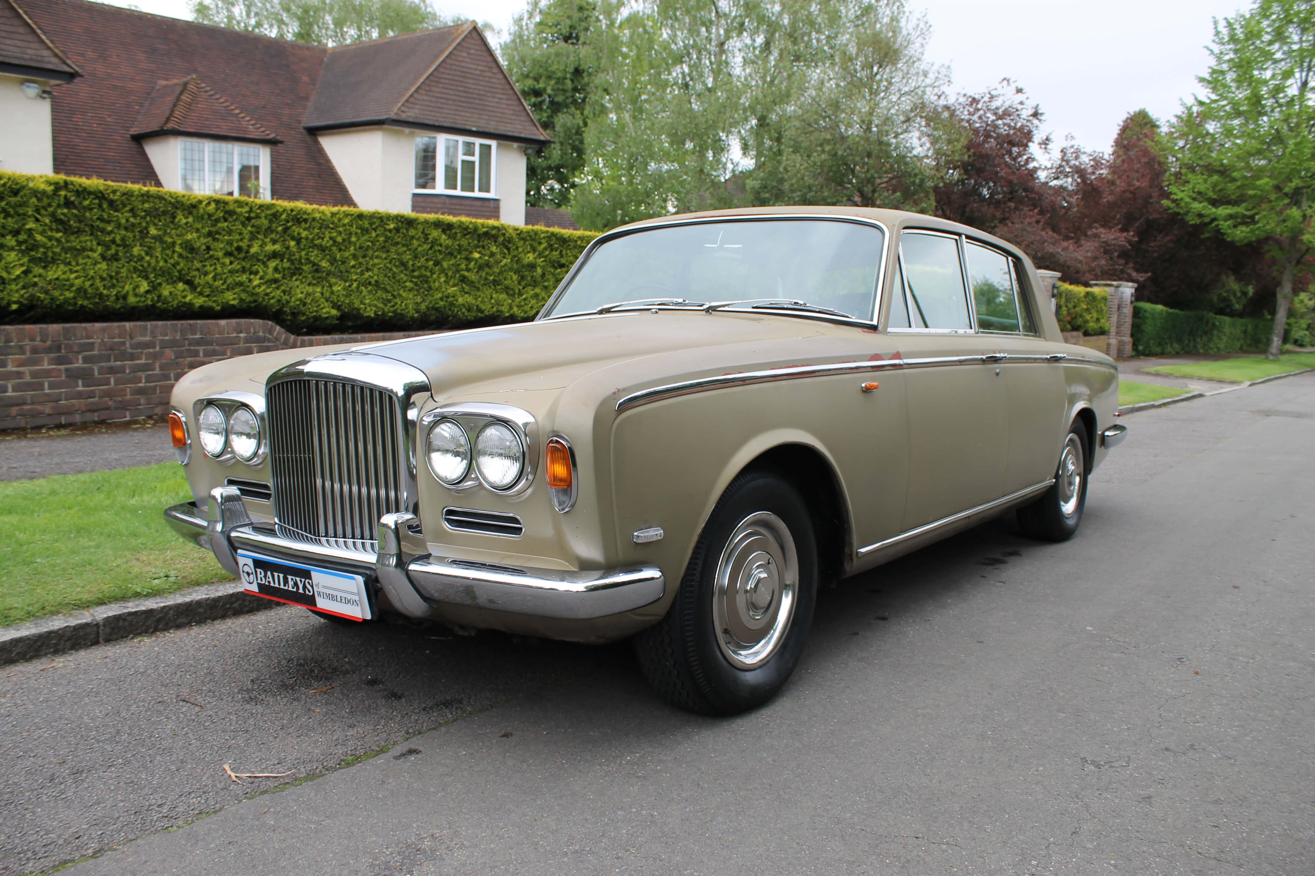 Bentley T1 桌布 壁紙 — 一輛經典米色賓利S1轎車停放在寧靜的住宅街道上，背景有綠色樹籬和磚造房屋。