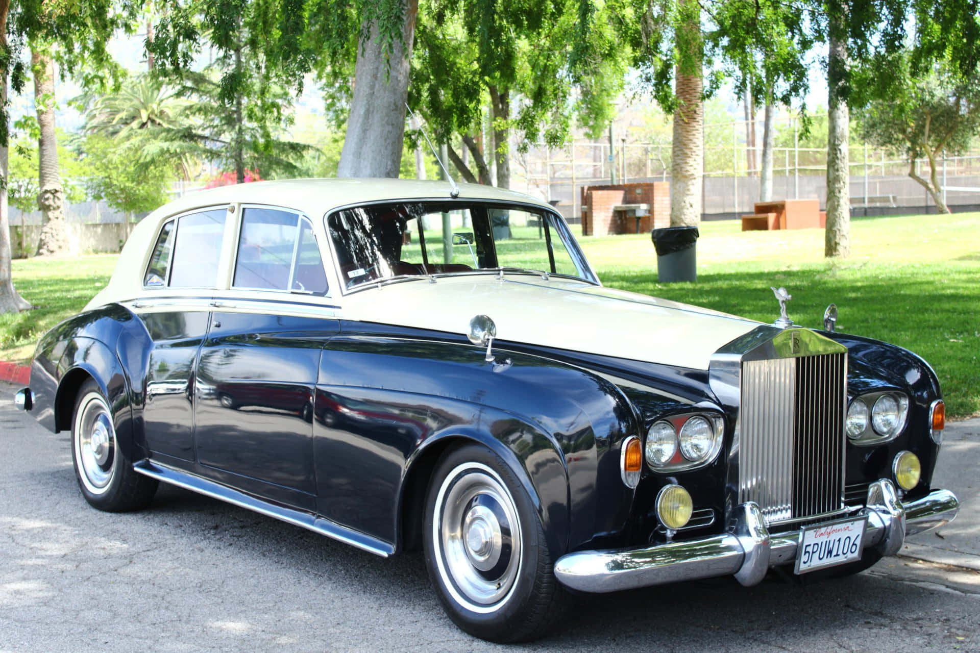 Bentley S3 桌布 壁紙 — 一輛經典的黑白勞斯萊斯優雅地停在陽光明媚的公園車道上，周圍環繞著茂密的綠樹。