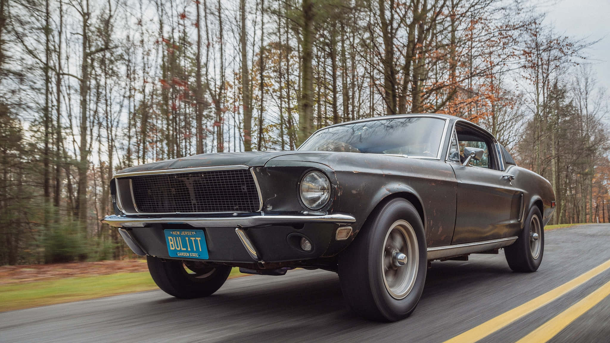 Ford Mustang Bullitt 桌布 壁紙 — 經典黑色福特野馬 Bullitt 在森林道路上巡航，秋天的樹木模糊掠過。