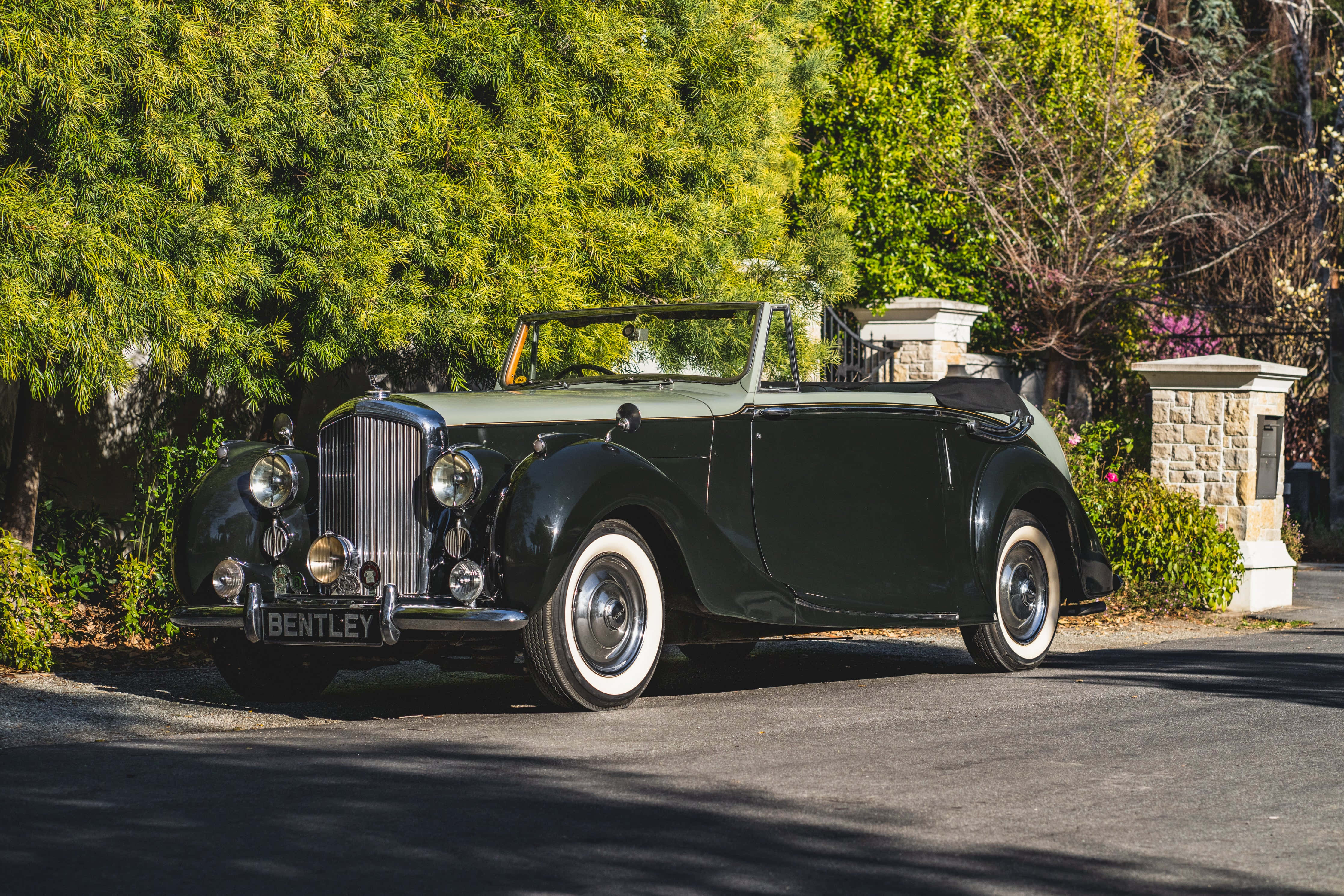 Bentley Mark Vi 桌布 壁紙 — 一輛經典綠色賓利敞篷車停放在陽光普照的車道上，旁邊是茂密的綠色樹籬和石柱。