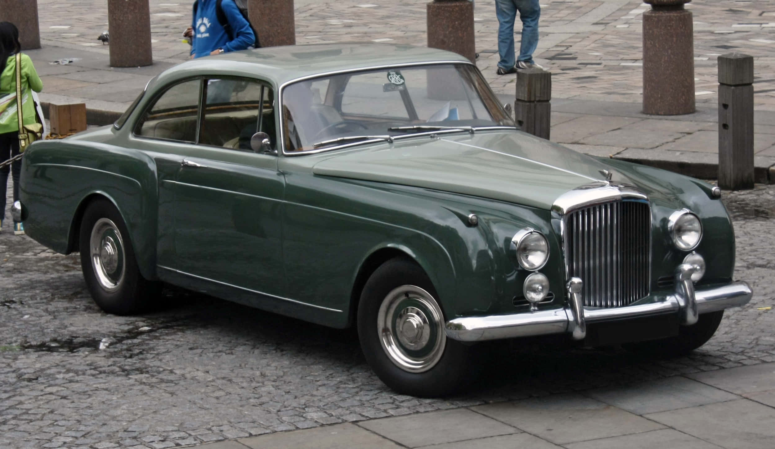 Bentley S2 桌布 壁紙 — 一輛經典綠色賓利轎車停放在濕漉漉的鵝卵石街道上，附近有行人。