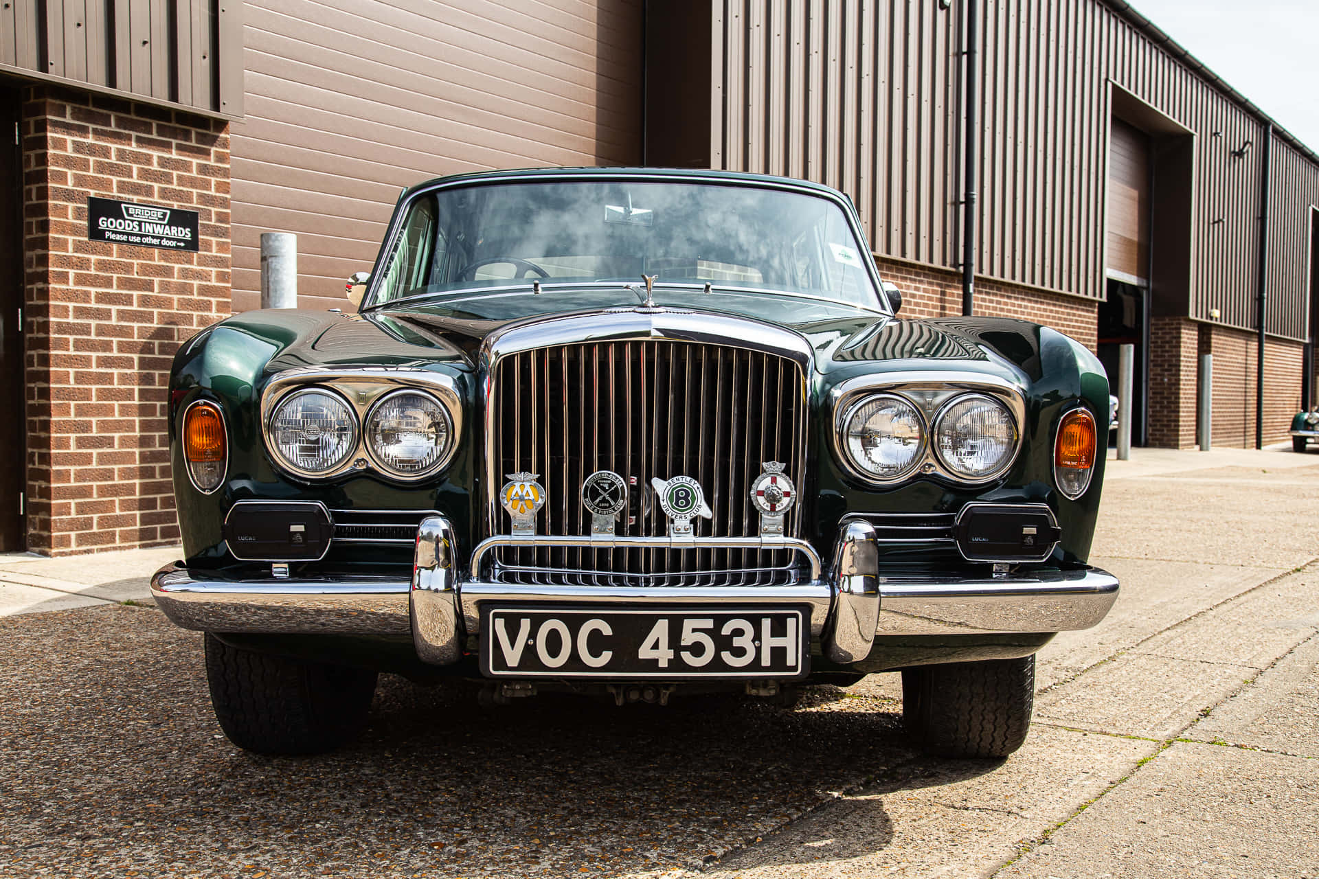 Bentley T1 桌布 壁紙 — 一輛經典綠色賓利，帶有鍍鉻格柵和圓形頭燈，停在磚和金屬建築前。
