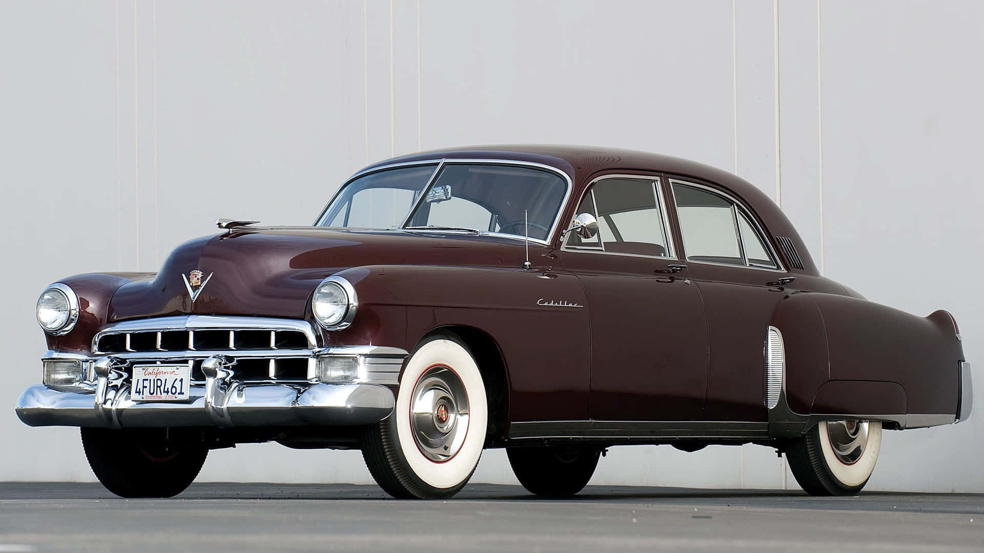 Cadillac Fleetwood 桌布 壁紙 — 一輛經典的1940年代栗色凱迪拉克轎車，帶有鍍鉻裝飾和白牆輪胎，停在簡約的灰色牆壁前。