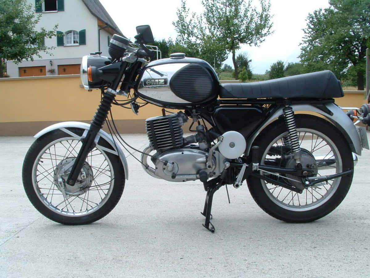 Mz Motorcycle 桌布 壁紙 — 一輛經典銀黑色Oriz機車停放在混凝土車道上，背景有房屋和樹木。
