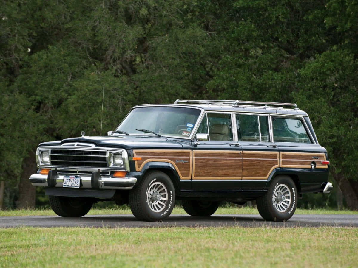 Jeep Wagoneer 桌布 壁紙 — 一輛經典的木質鑲板Jeep Wagoneer停在草地路邊，背景是茂密的綠樹。