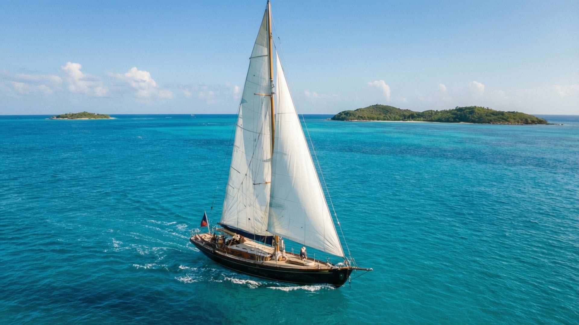 Caribbean Sailing Yacht 壁紙 — 一艘經典木製帆船，白色風帆，在清澈藍天下，於碧綠島嶼附近生動的藍綠色海水中滑行。