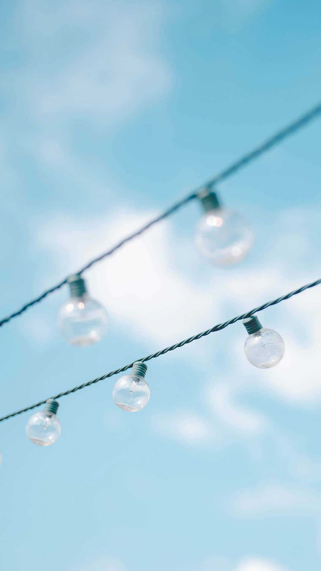  壁紙 — 透明玻璃燈串斜掛在帶有縷縷白雲的柔和藍天上。
