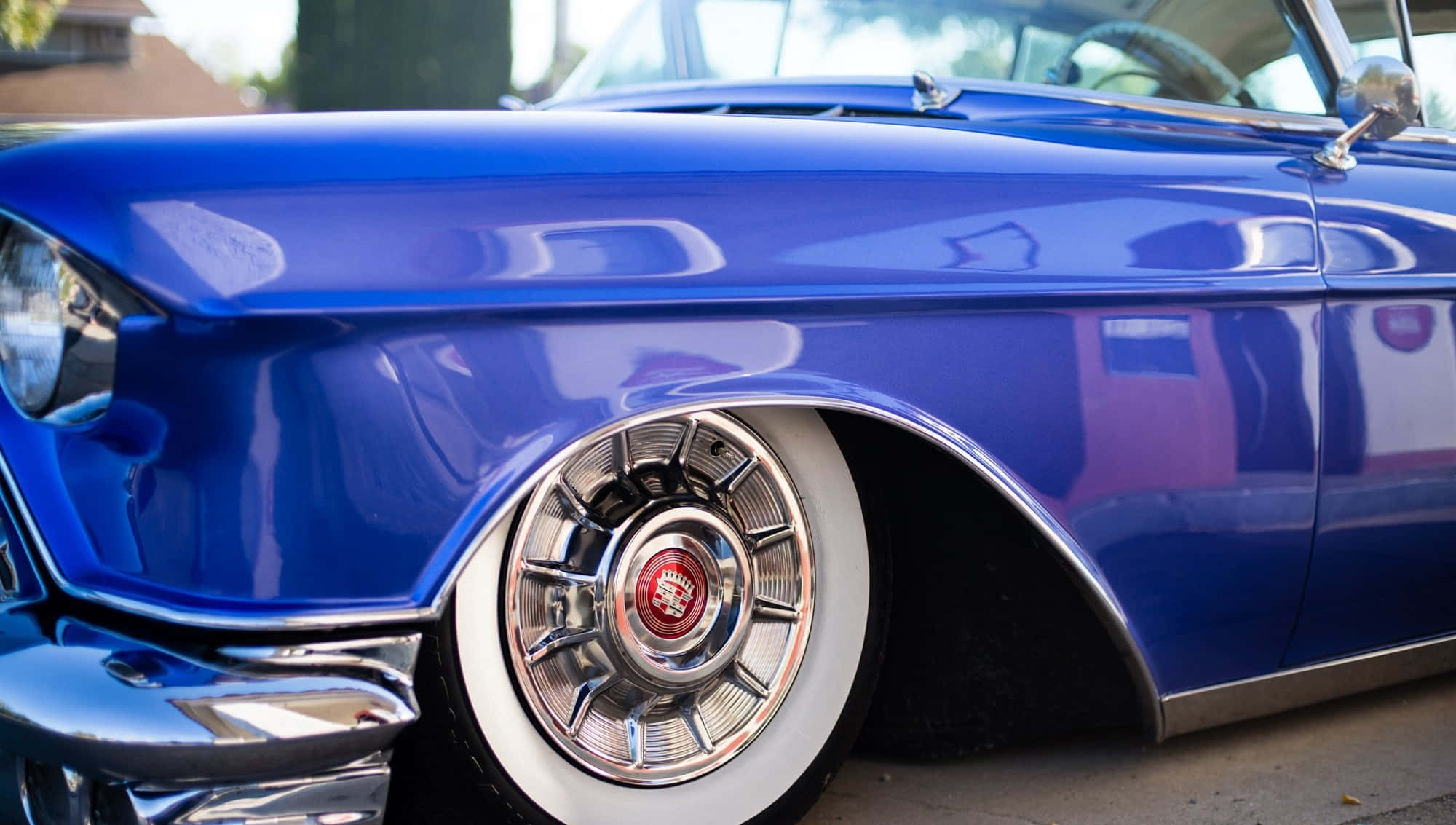 Cadillac Deville 桌布 壁紙 — 一輛光澤藍色經典汽車的前擋泥板和鍍鉻輪圈搭配白邊輪胎的特寫。