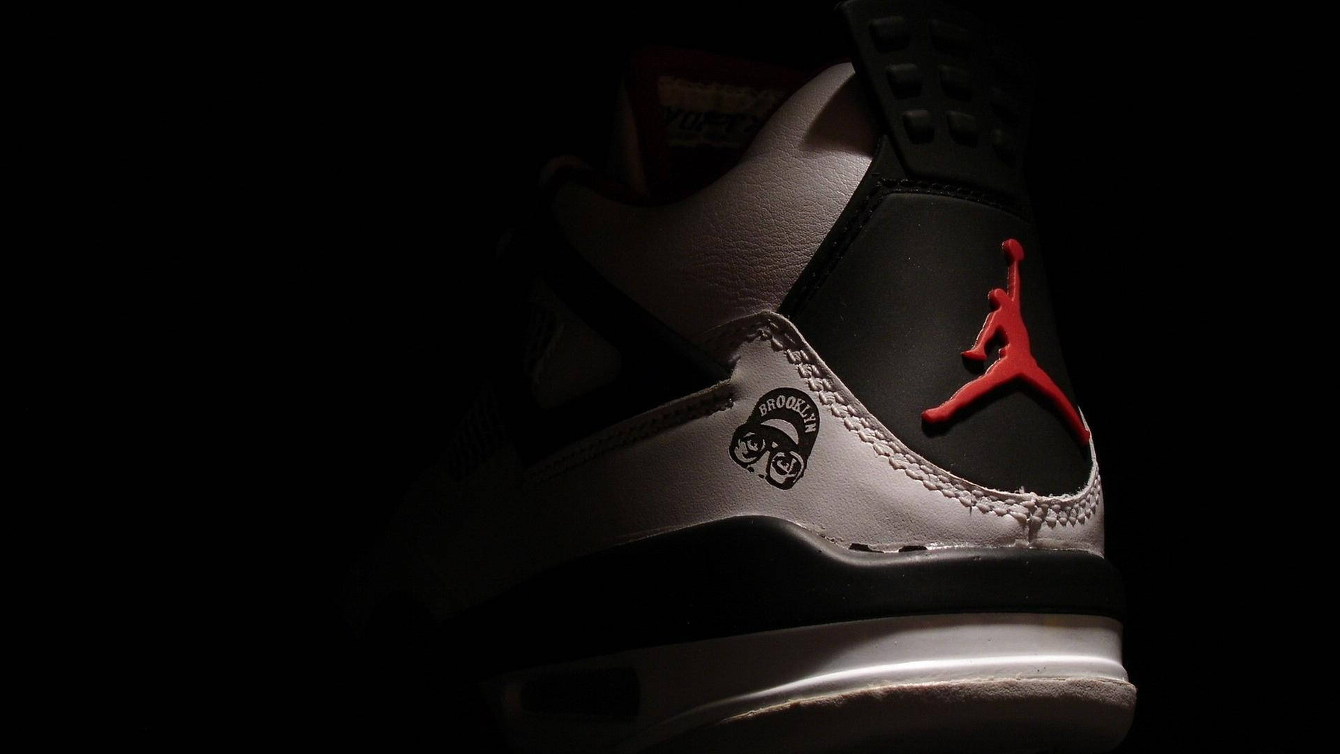 一雙在昏暗光線下帶有紅色標誌的黑白 Jordan 運動鞋。 — Jordan Logo 壁紙