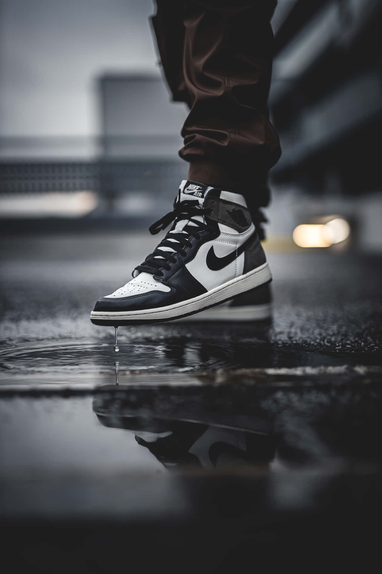 一雙黑白運動鞋在都市環境中將水滴落在濕漉漉的路面上。 — Air Jordan 壁紙